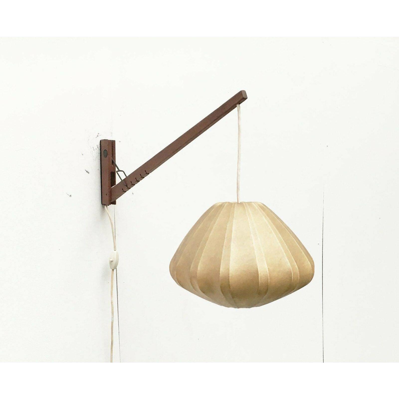 Elegant mid-century teak wall lamp with cocoon shade.

the light can be swiveled and tilted. A special detail is the manual adjustment of the arm of the lamp. This is functional and at the same time designed as a striking design element. The arm has
