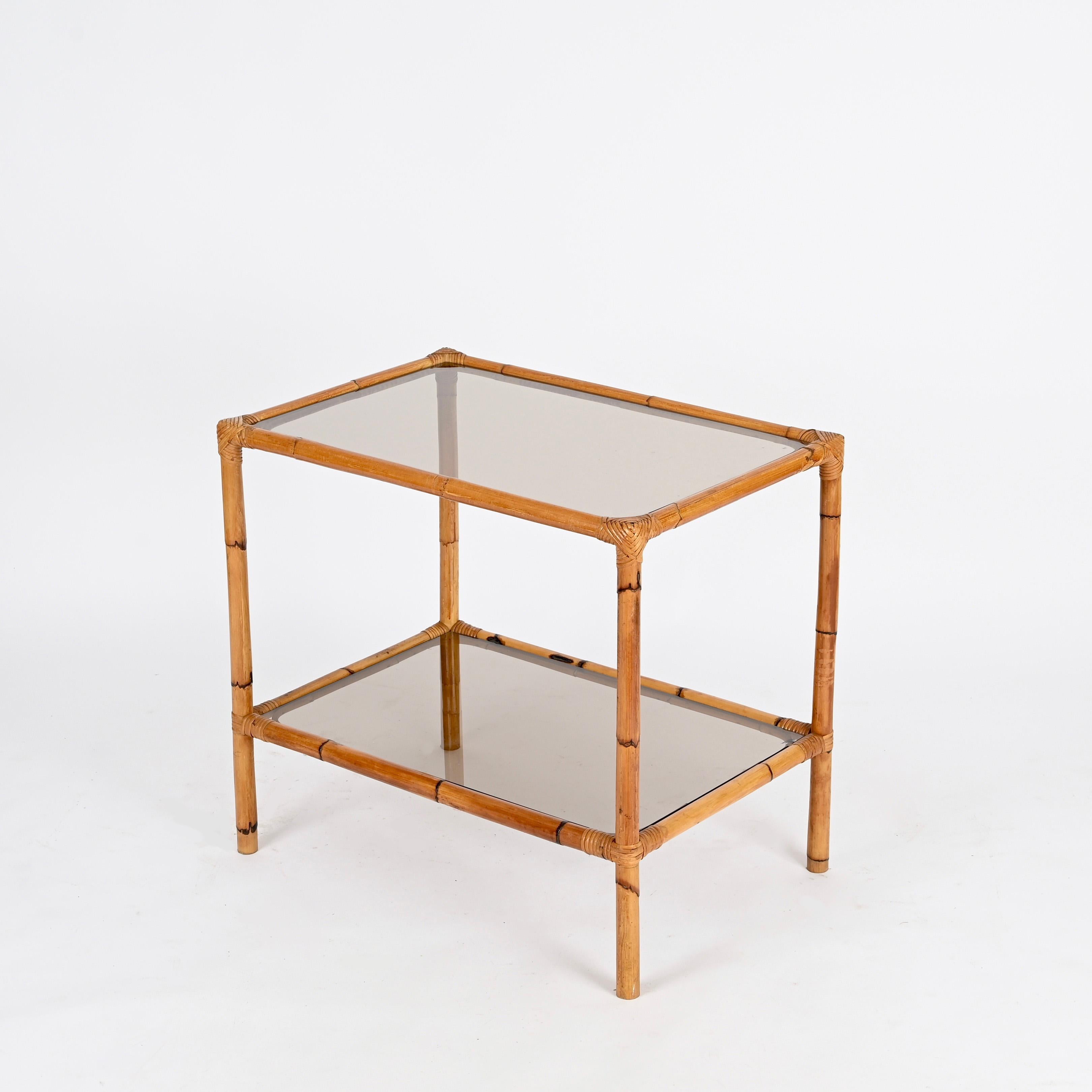Gorgeous mid-century organic two tier coffee or side table fully made in bamboo and hand-woven wicker with smoked glasses. This charming and unique piece was designed in Italy during the 1960s.  

In amazing condition and with a lovely dark honey