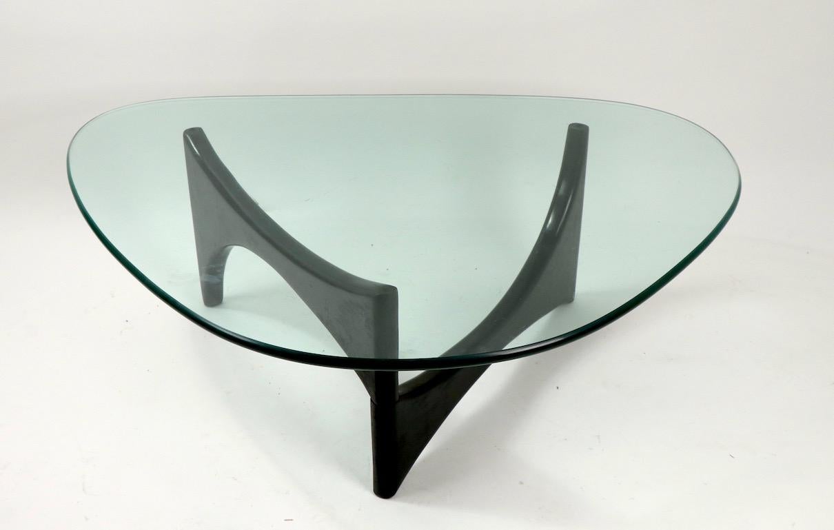 Classic glass top coffee table design after the iconic Noguchi design. Thick (.75 ) plate glass top rests on adjustable wood base. The top is free of chips or cracks, it does show minor surface scratches, inconsequential, and consistent with age.