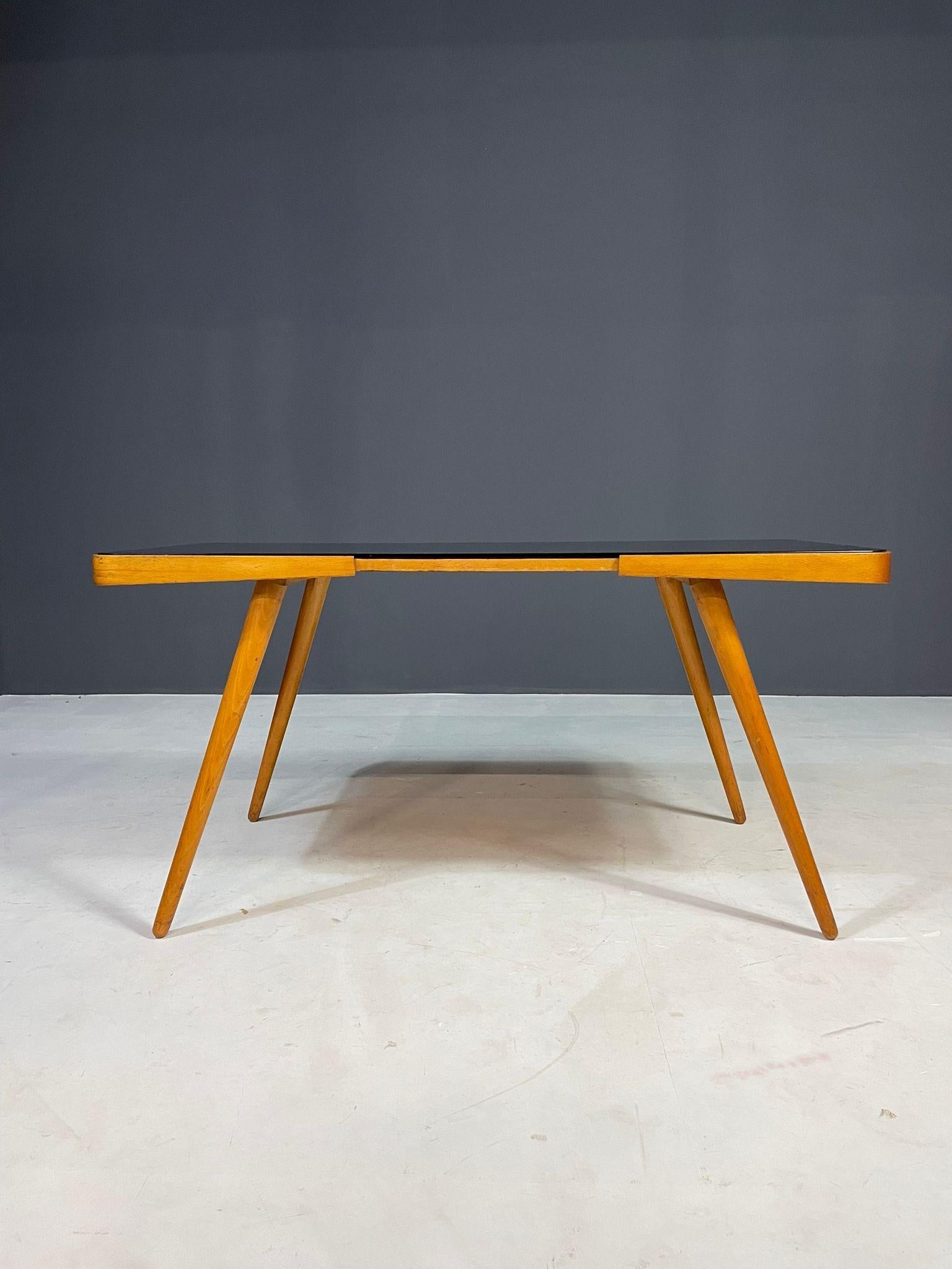 Mid-century coffee table produced by Interiér Praha in former Czechoslovakia during the 1960s. This piece showcases a classic Czech design aesthetic, featuring a sleek black opaxite glass top and angled wooden legs that enhance its elegant and