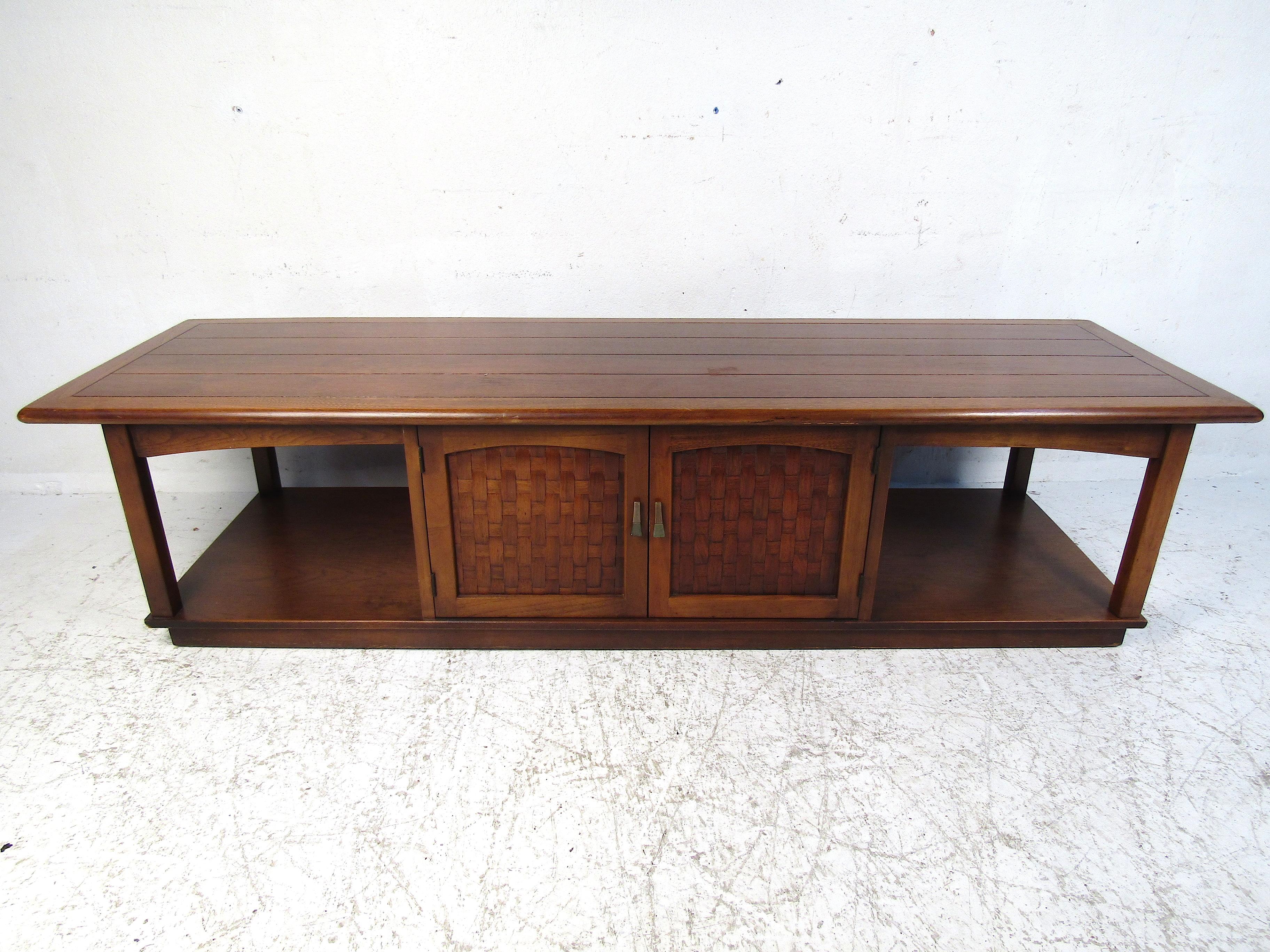 Nice midcentury coffee table by Lane Furniture Co. Interesting design with two tiers, rounded edges, and a storage compartment. Woven accents on the cabinet door-fronts.