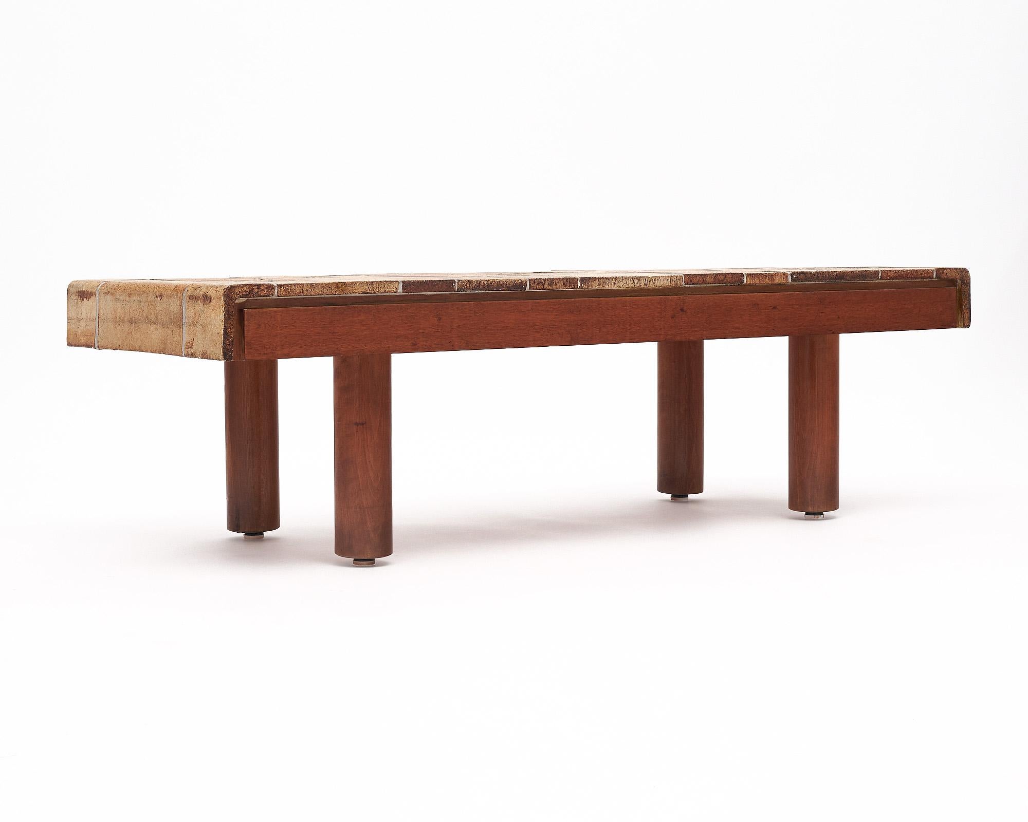 Table basse de France par Roger Capron. La structure est en bois avec des pieds cylindriques. Il est surmonté d'un plateau carrelé et incurvé. Les carreaux présentent des détails de la nature, notamment des feuilles et des fleurs. Le tableau est