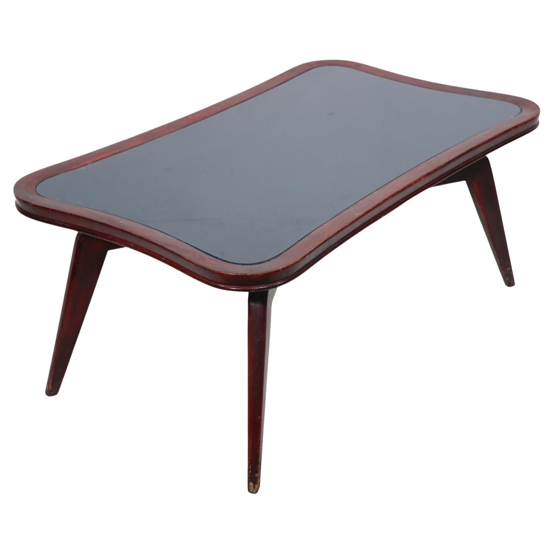 Voguish, chic, architectural mid century coffee table, having a floating organic form top, on tapering spider style legs. The table top features an insert glass surface in an intriguing dark green color, which rests in the corresponding oak frame.