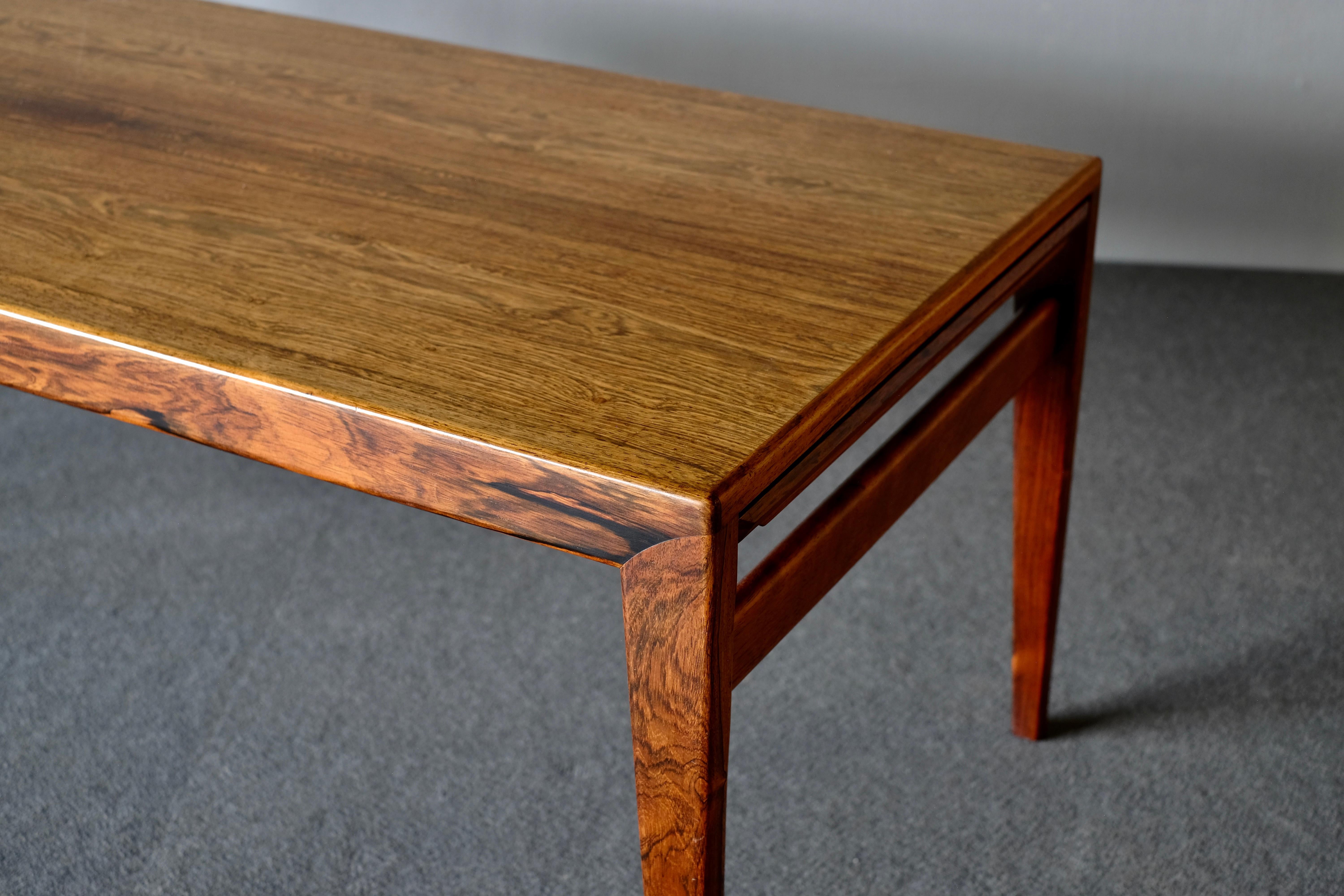 Midcentury coffee table by Johannes Anderson in Brazilian rosewood. The patina and the wonderful grain pattern of the wood on this elegant table make it very special. It has a clever pull-out leaf of black Formica on either end of the table.