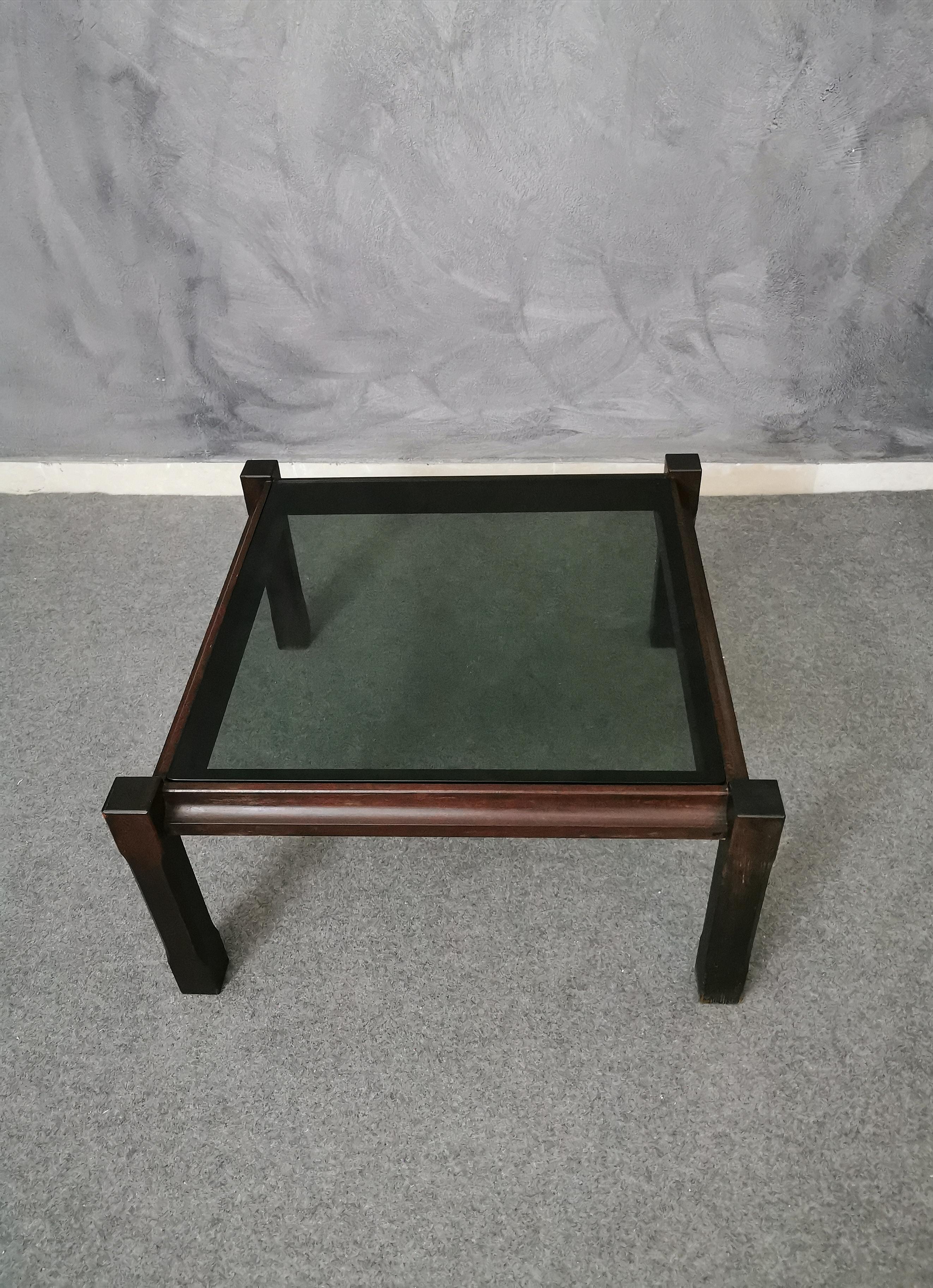 Square wood coffee table with removable smoked glass top. The coffee table has 4 wooden feet that protrude slightly in the part of the glass top, Italian production of the 1960s.