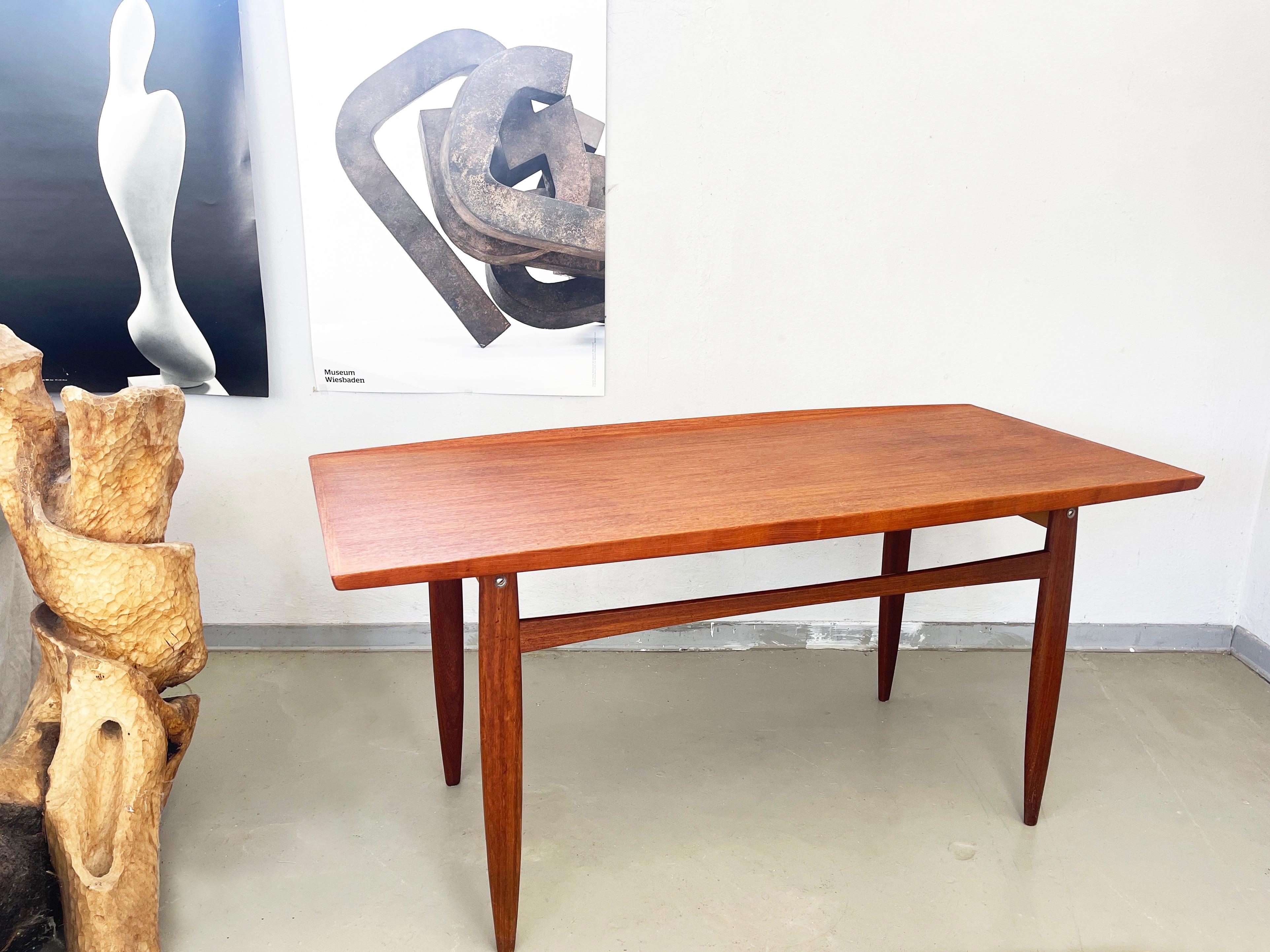Table basse d'après ou par Grete Jalk en teck brun chaud magnifiquement travaillé.
Fabriqué au Danemark ou en Allemagne vers 1960.
Belle forme allongée, légèrement conique vers les extrémités longues, les côtés sont en relief. 
merveilleusement
