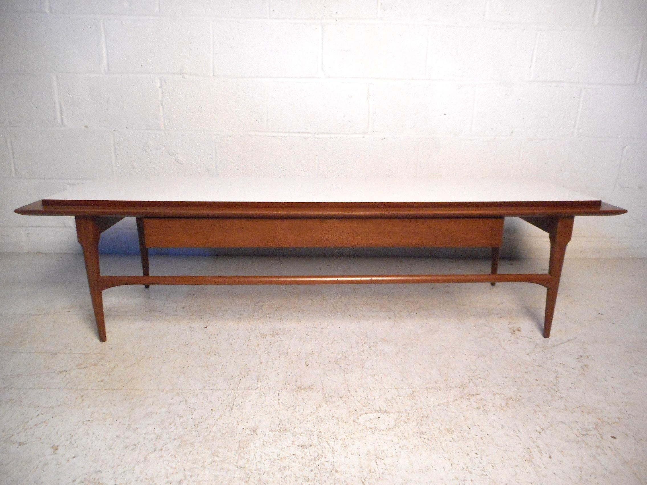 Impressive midcentury coffee table featuring a white laminate top, sleek tapered legs and stretchers, and a singe wide drawer offering storage space. A great addition to any modern interior. Please confirm item location with dealer (NJ or NY).