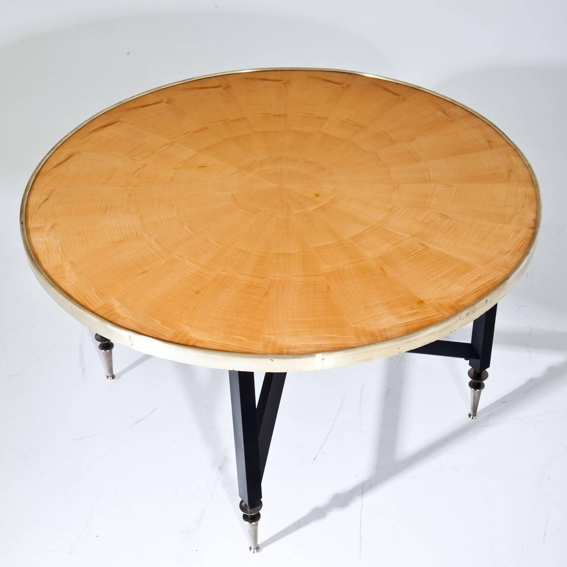 Round Midcentury coffee table on a black steel base with conical metal feet. The tabletop has a brass border and shows a beautiful maple veneer. prob. Italy