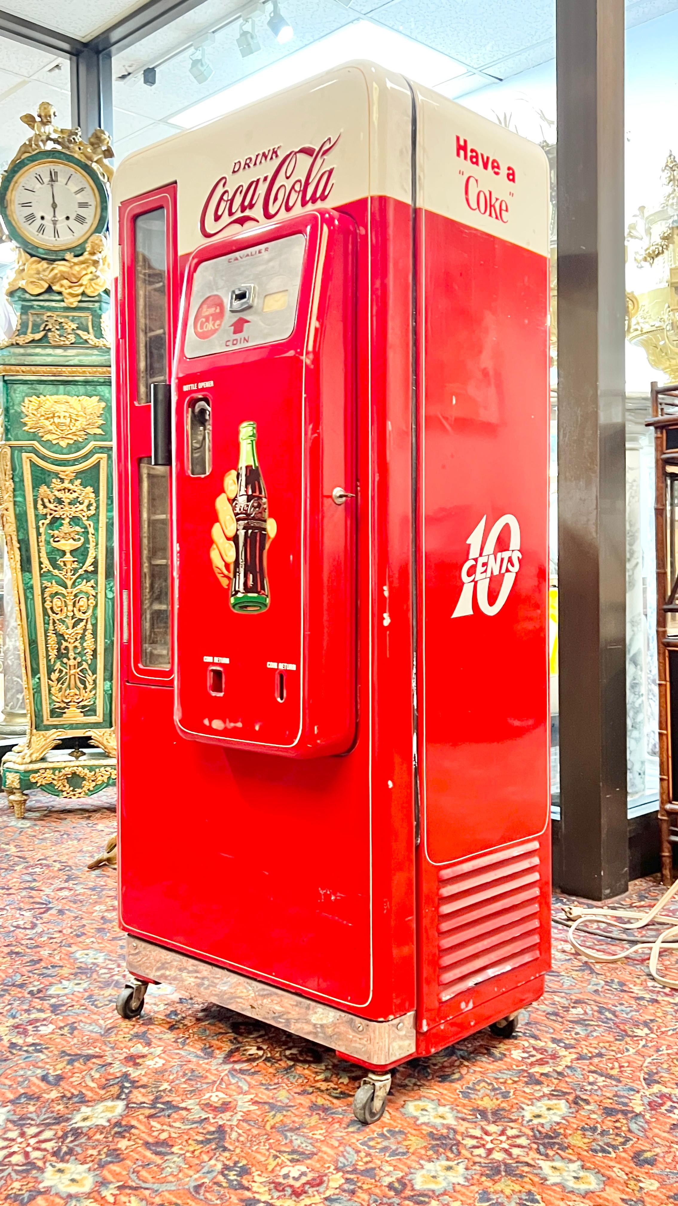 Distributore automatico di coca-cola d'epoca, modello Cavalier 72, risalente alla fine degli anni '50-'60, misura 59 x 25 x 21 pollici.  Montato su rotelle.  Circa 240 libbre.

Questo modello contiene 72 bottiglie e ha il meccanismo originale delle