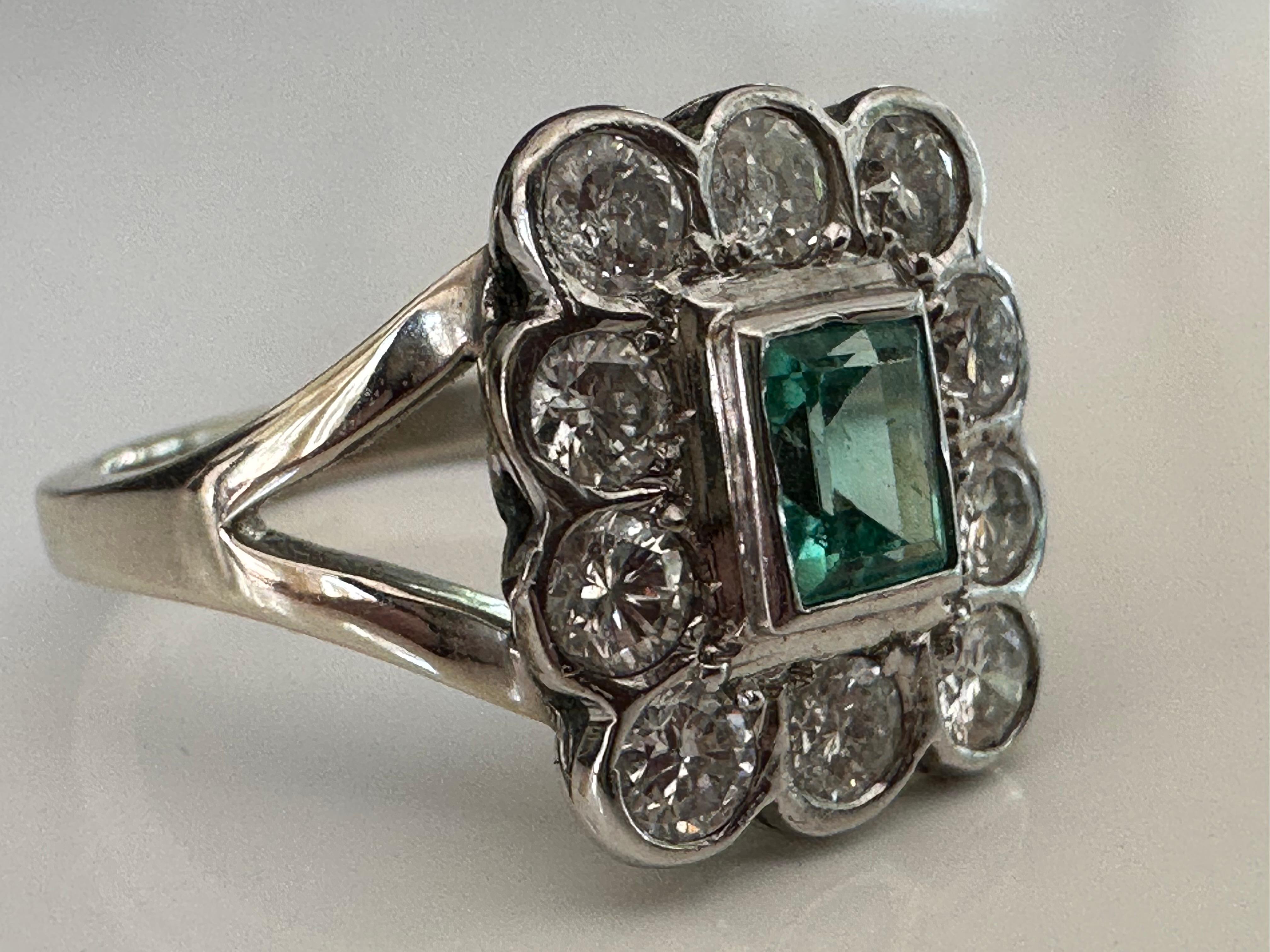 Crafted in the 1950s, this mid-century ring features a 0.70-carat Colombian emerald center stone framed by ten round brilliant-cut diamonds totaling 1.00 carat. Set in platinum with a split shank and band handcrafted in 14K white gold. 
