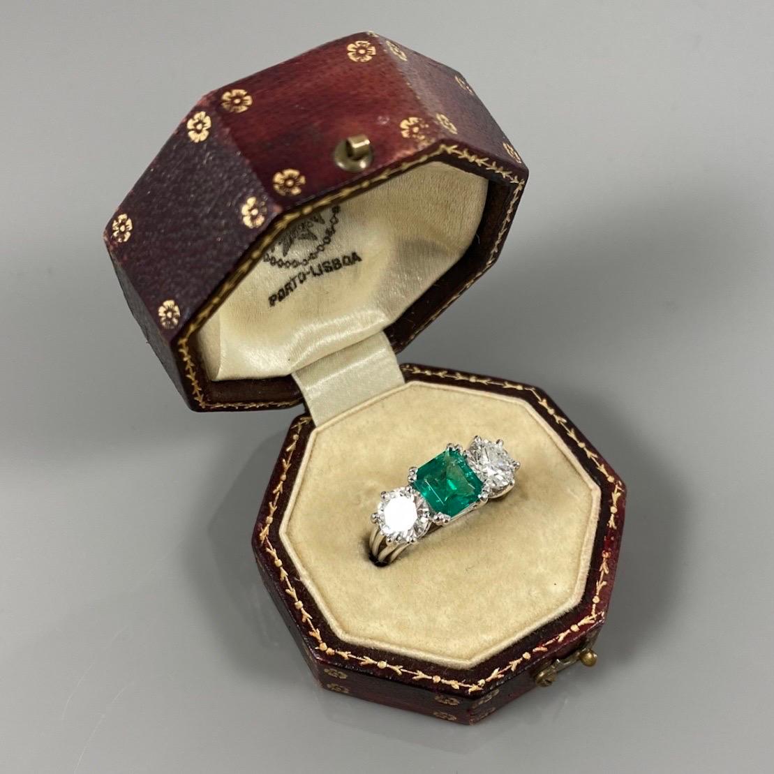 Mid-Century certified Colombian emerald and diamond three-stone engagement ring in platinum, Portuguese, 1950s/1960s, Cased. This ring features an octagonal-cut emerald of a vivid green color claw-set to the center, flanked on each side by a