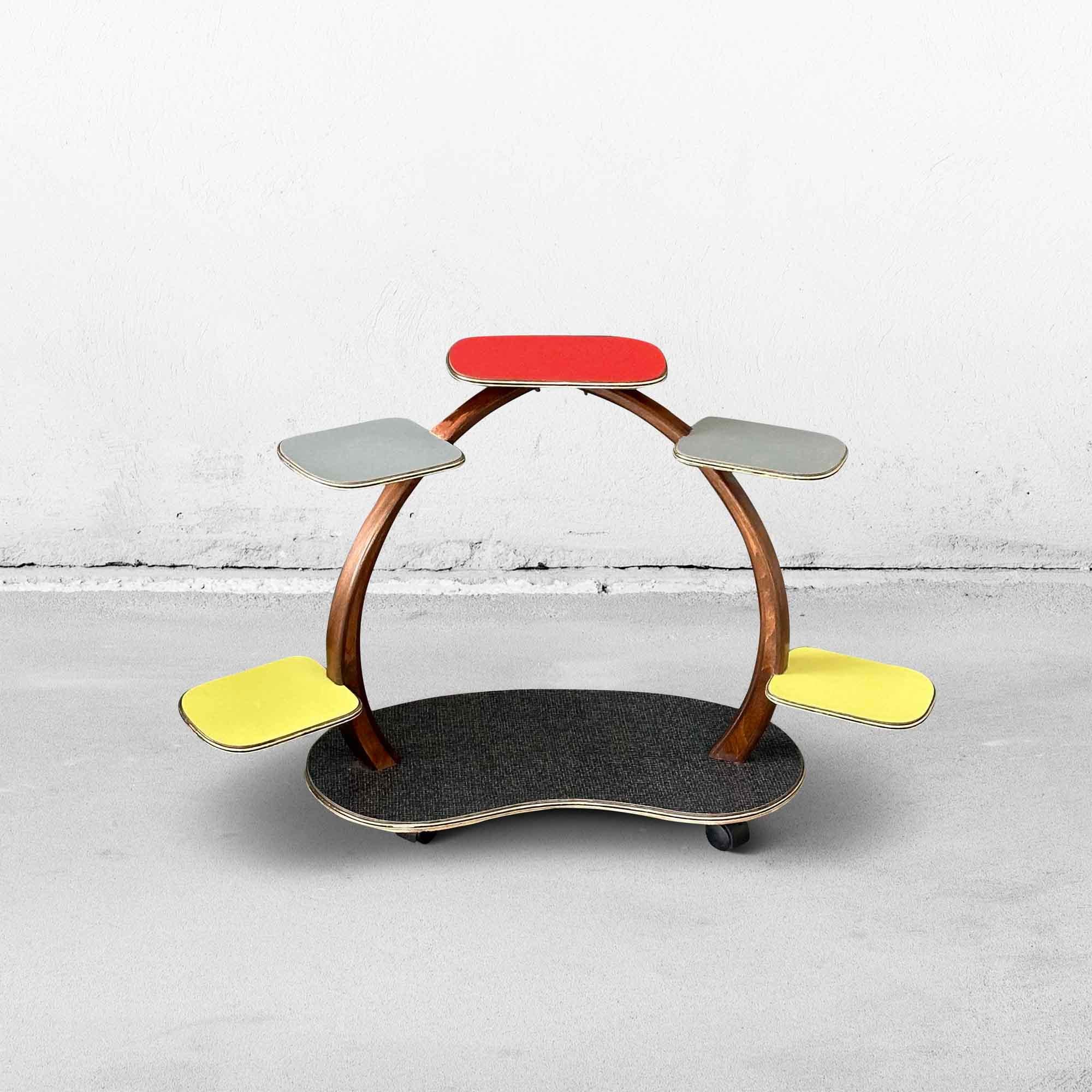 Mid-century plant stand from the 1960s. This colorful little table is made of wood and Formica in yellow, gray, red, and dark gray with a pattern. The shelves have the typical gold-colored band. The wood has been restored at the top. The special