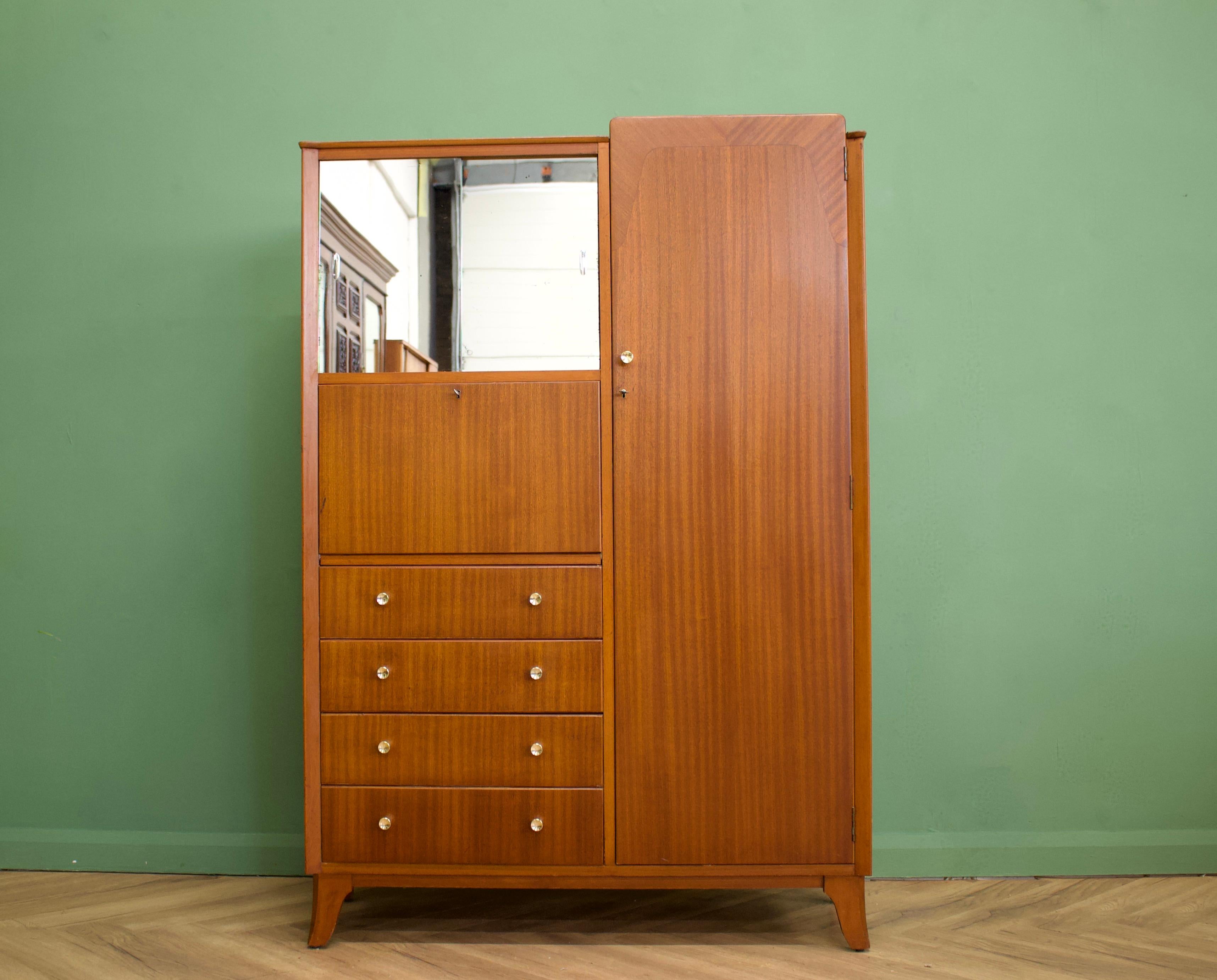 A compact teak wardrobe from Lebus.
Featuring a hanging rail, mirrored sliding door compartment, a drop down door cabinet and four drawers
Two doors are lockable.
The handles are solid brass.
This piece could be used as a hall storage