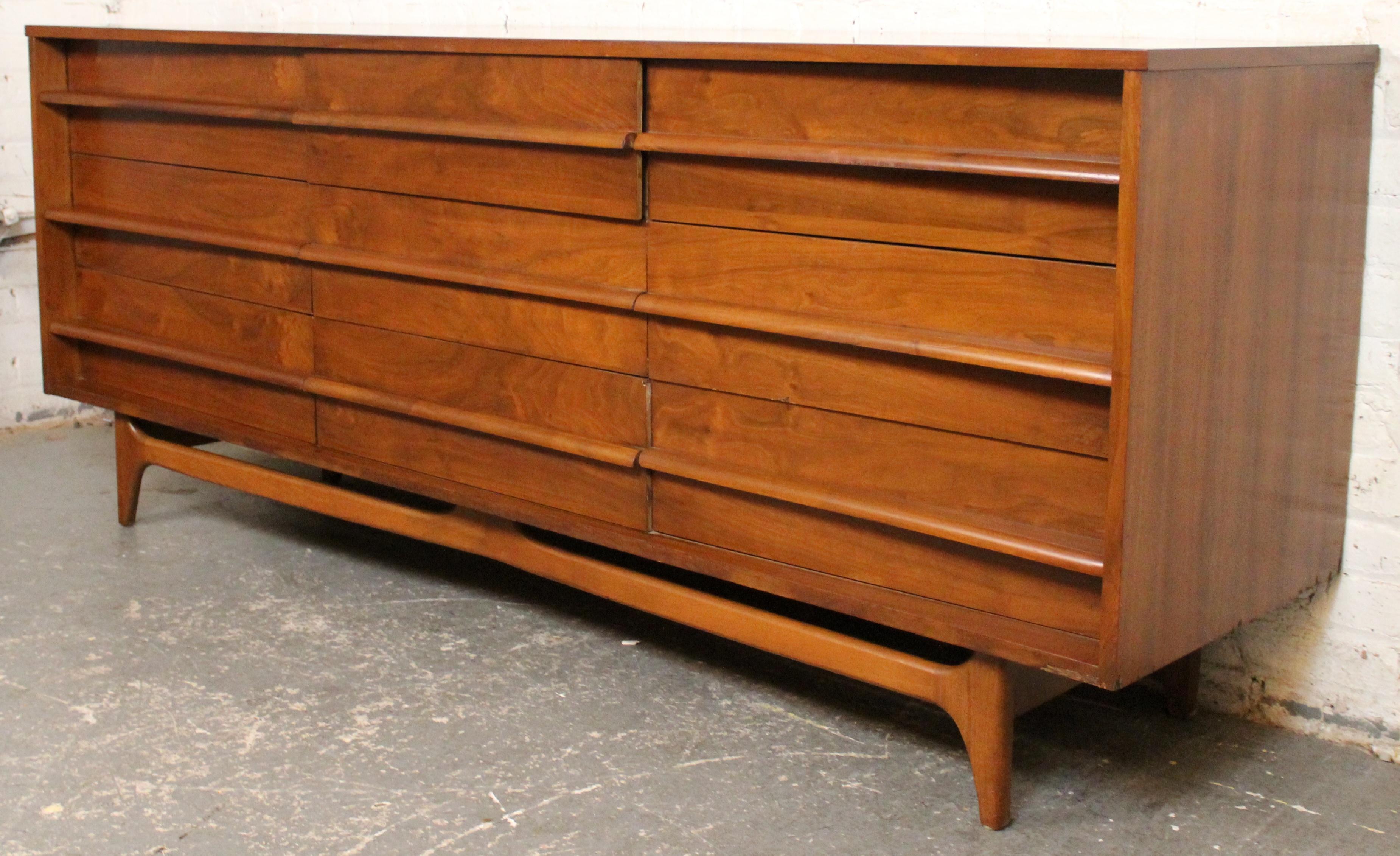 Elegante comò della metà del secolo scorso di Young Manufacturing Co. caratterizzato da un esclusivo frontale concavo e da una struttura in noce ricca di venature. Disegnato con linee pulite e tiretti scolpiti, questo pezzo degli anni '60 offre nove