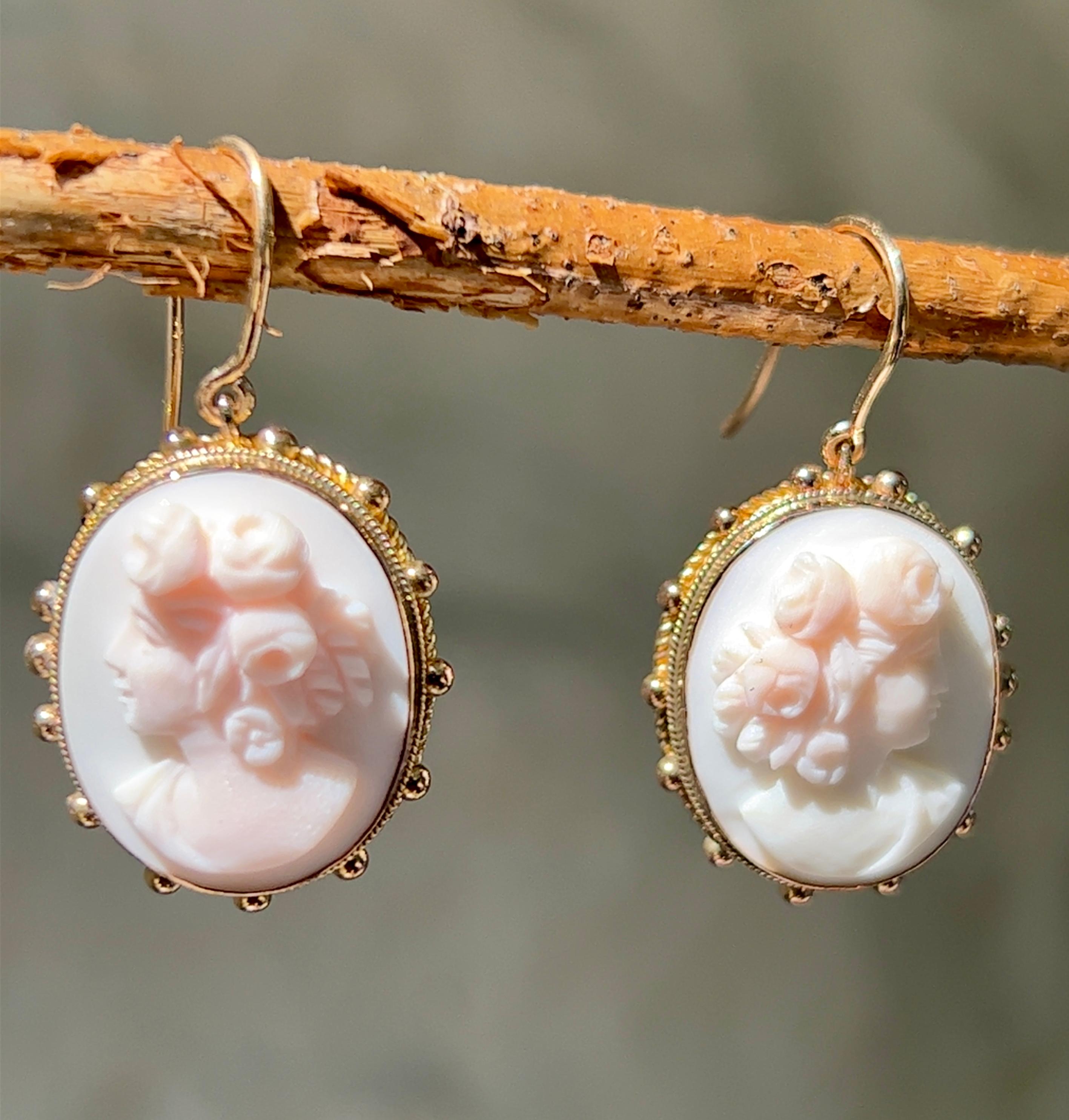 One pair of 14-karat yellow gold pink conch shell cameo earrings measuring 1.25 inches long and 0.75 of an inch wide. The earrings are complete with traditional hook closures.
