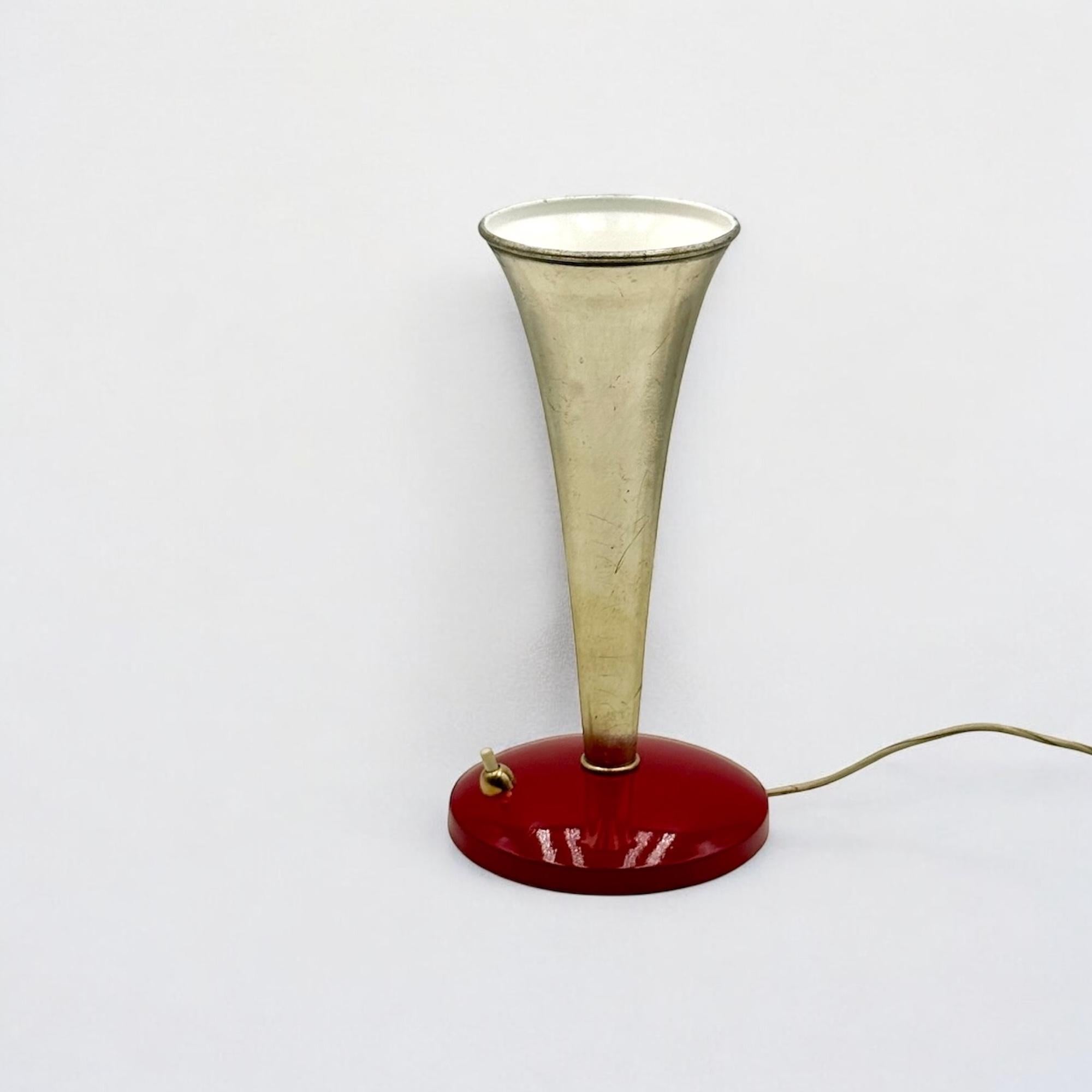 This Italian Mid Century Table Lamp, dating back to the 1950s/1960s, is a prime example of functional yet stylish design. The heavy, red enameled cast iron base ensures stability, while the conical metal shade-golden on the outside and