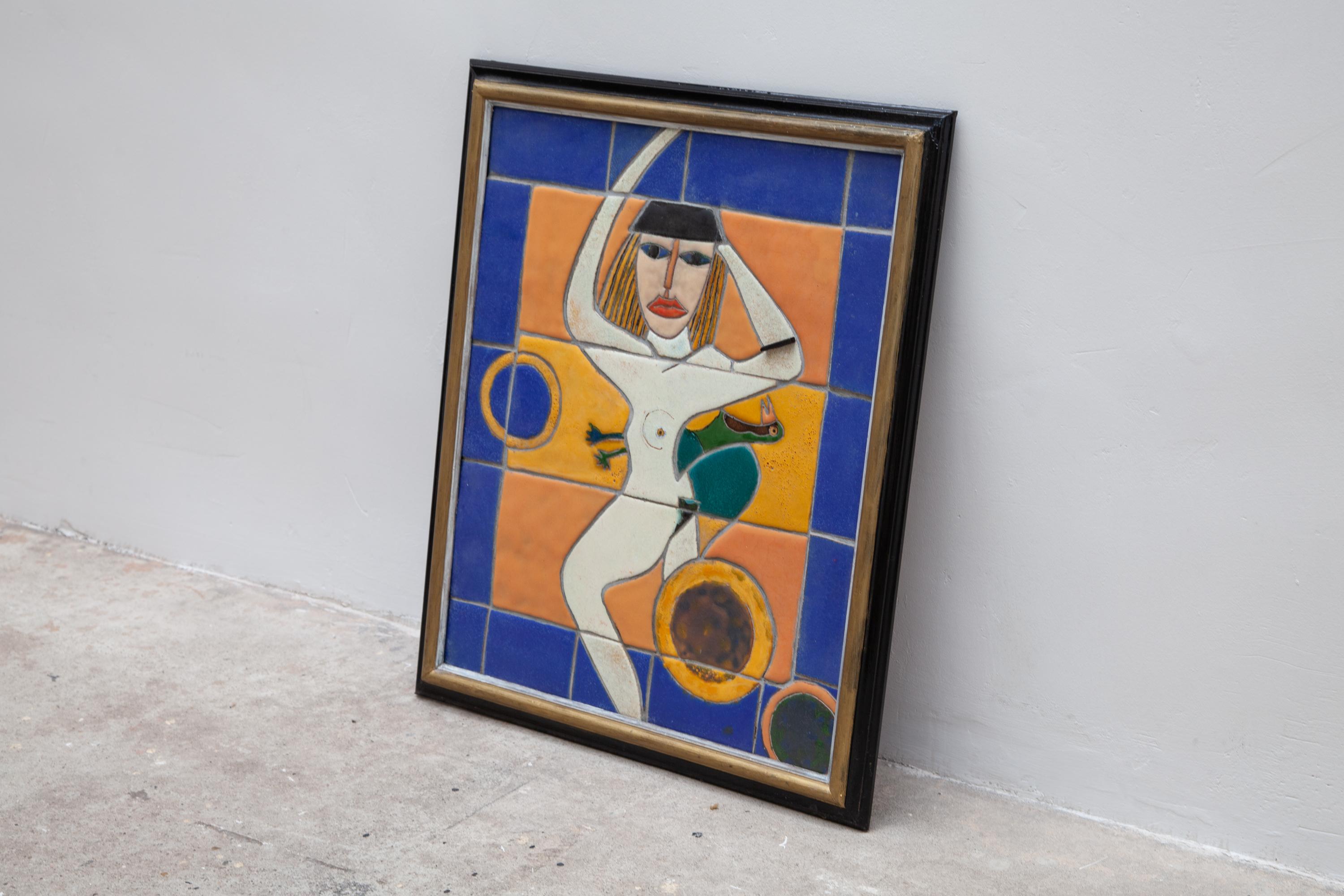 Vintage ceramic tile artwork featuring an abstract design of a woman with a bird in cobalt-blue, white, black, brown, yellow, orange and green. Black and gold frame. 1990s, stunning hand painted work of art in glazed ceramic.
The panel is in