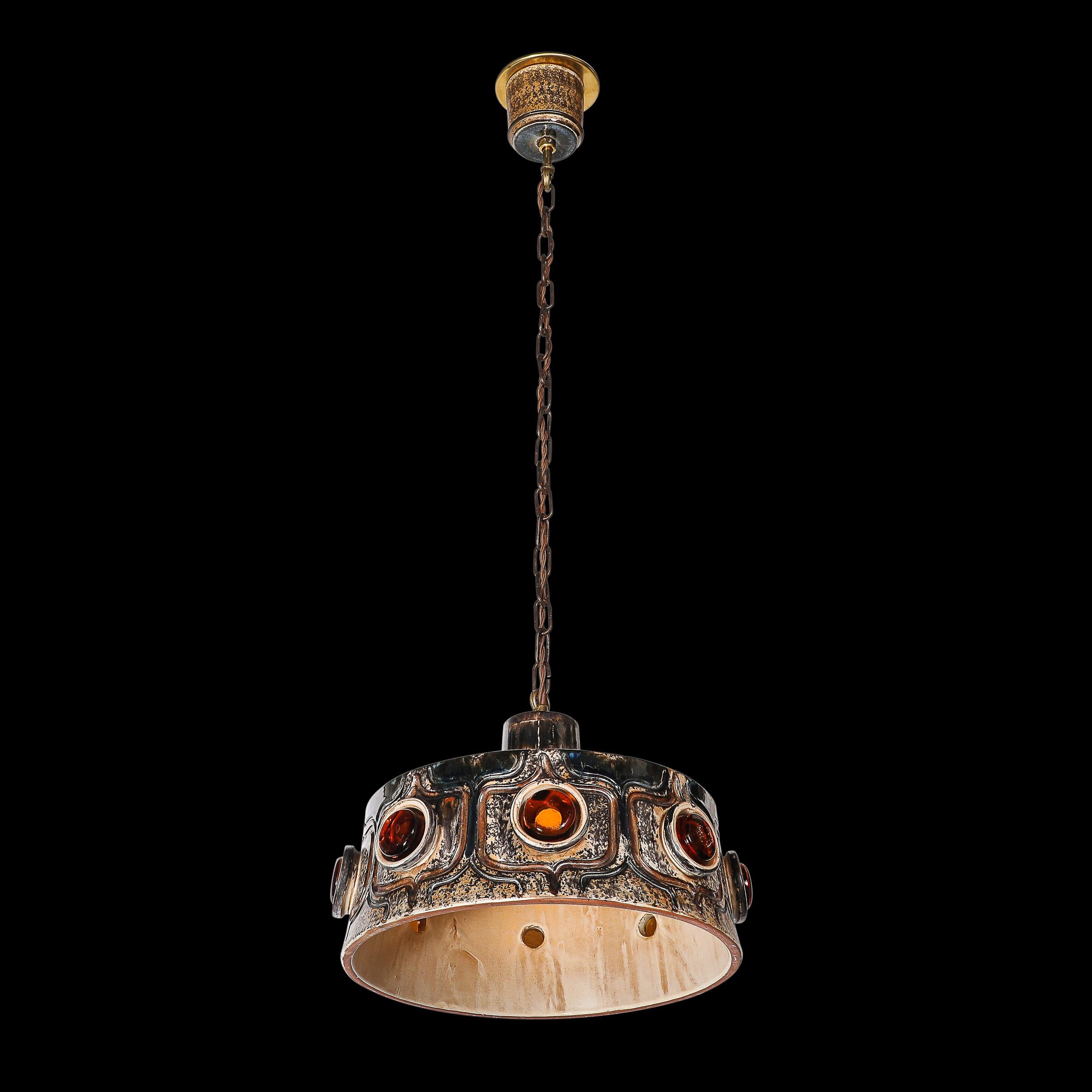 Esta elegante lámpara colgante modernista de mediados de siglo, fabricada en Francia hacia 1960, capta la sofisticación y la rigurosa artesanía características de la época. La araña presenta un cuerpo de cerámica ricamente esmaltada en un tono ámbar