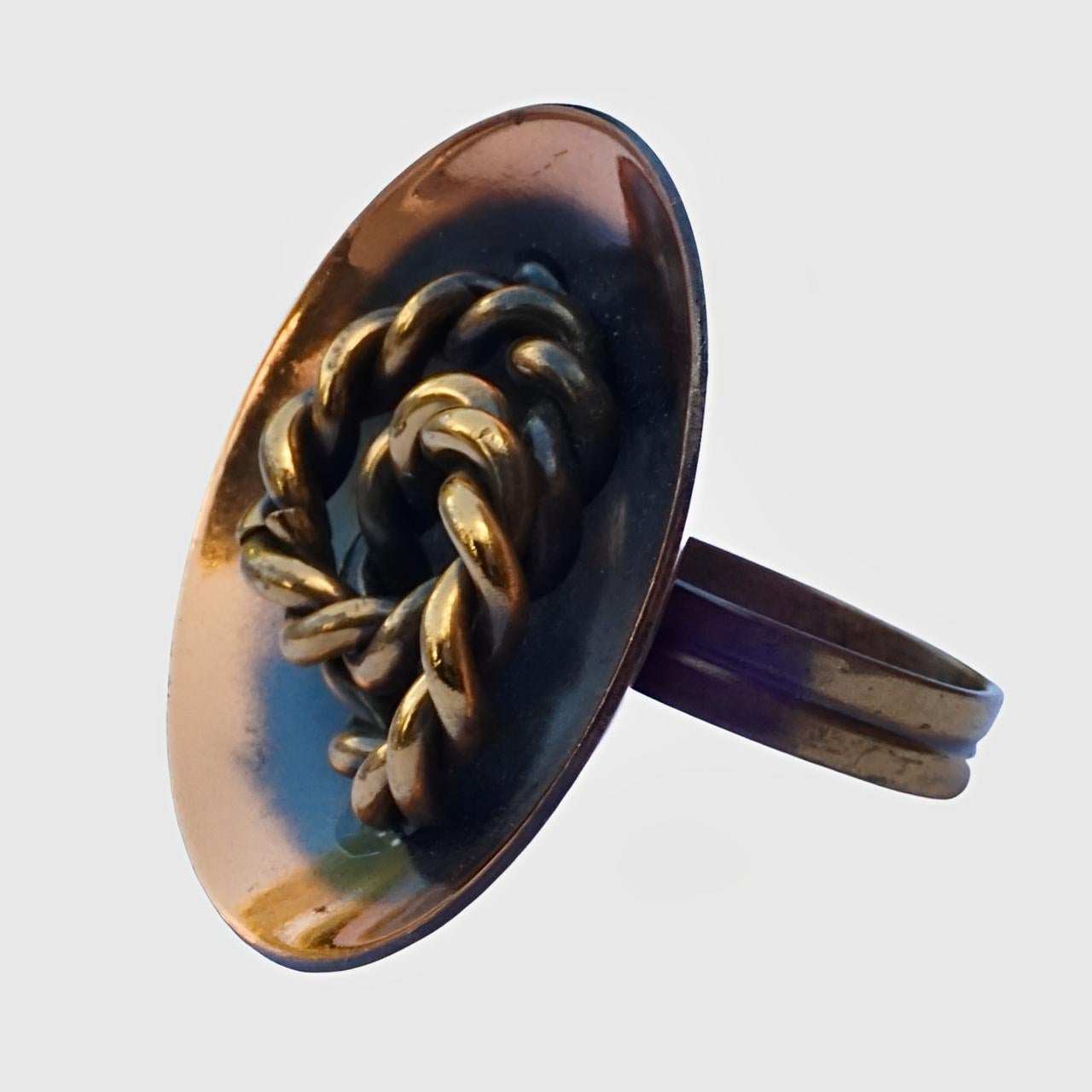 Anello rotondo in rame anodizzato lucido di metà secolo, caratterizzato da un disegno a corda ritorta in oro a contrasto. Anche la fascia è di colore oro. Il metallo dorato è probabilmente ottone.

Misura dell'anello UK Q / US 8, diametro interno
