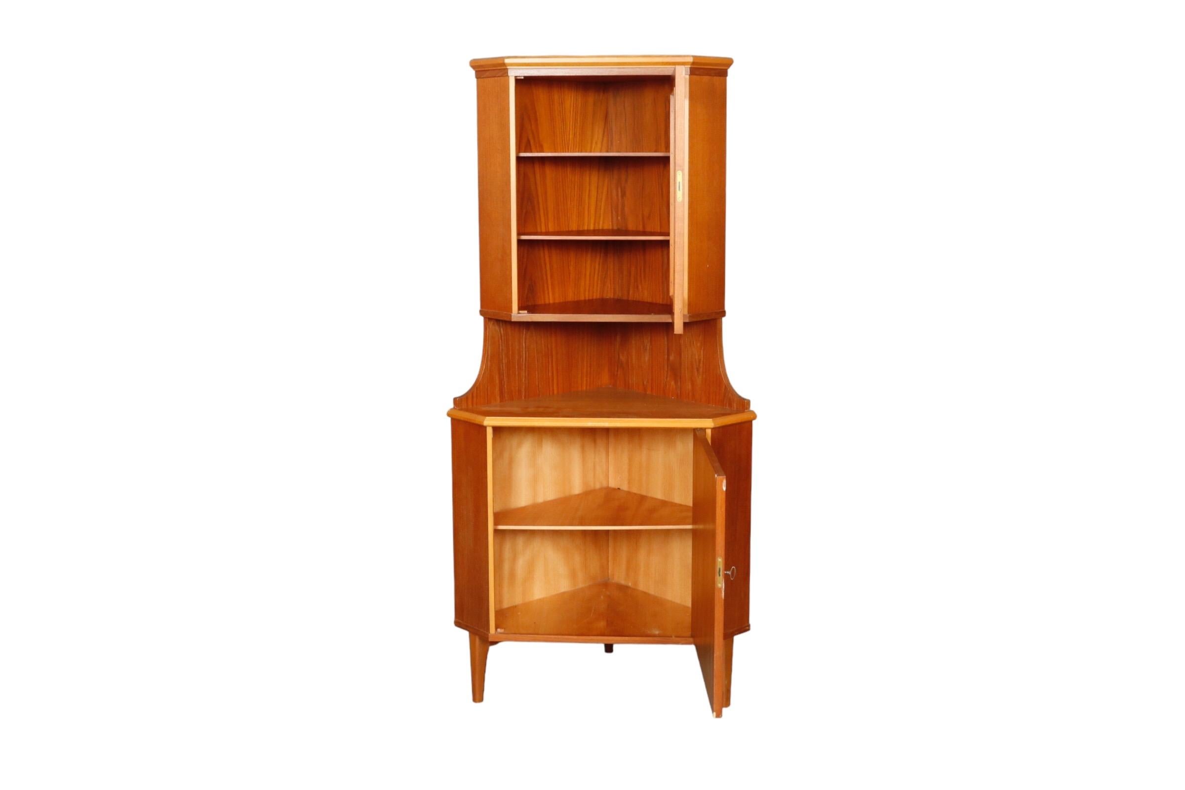 A 1970’s Danish corner cupboard with locking cabinets. The upper cabinet door has a glass panel decorated with a cartouche pattern. Inside are housed two shelves. The cabinet below houses a single shelf.

H:67.75” 
W:31.5” 
D:17.75”