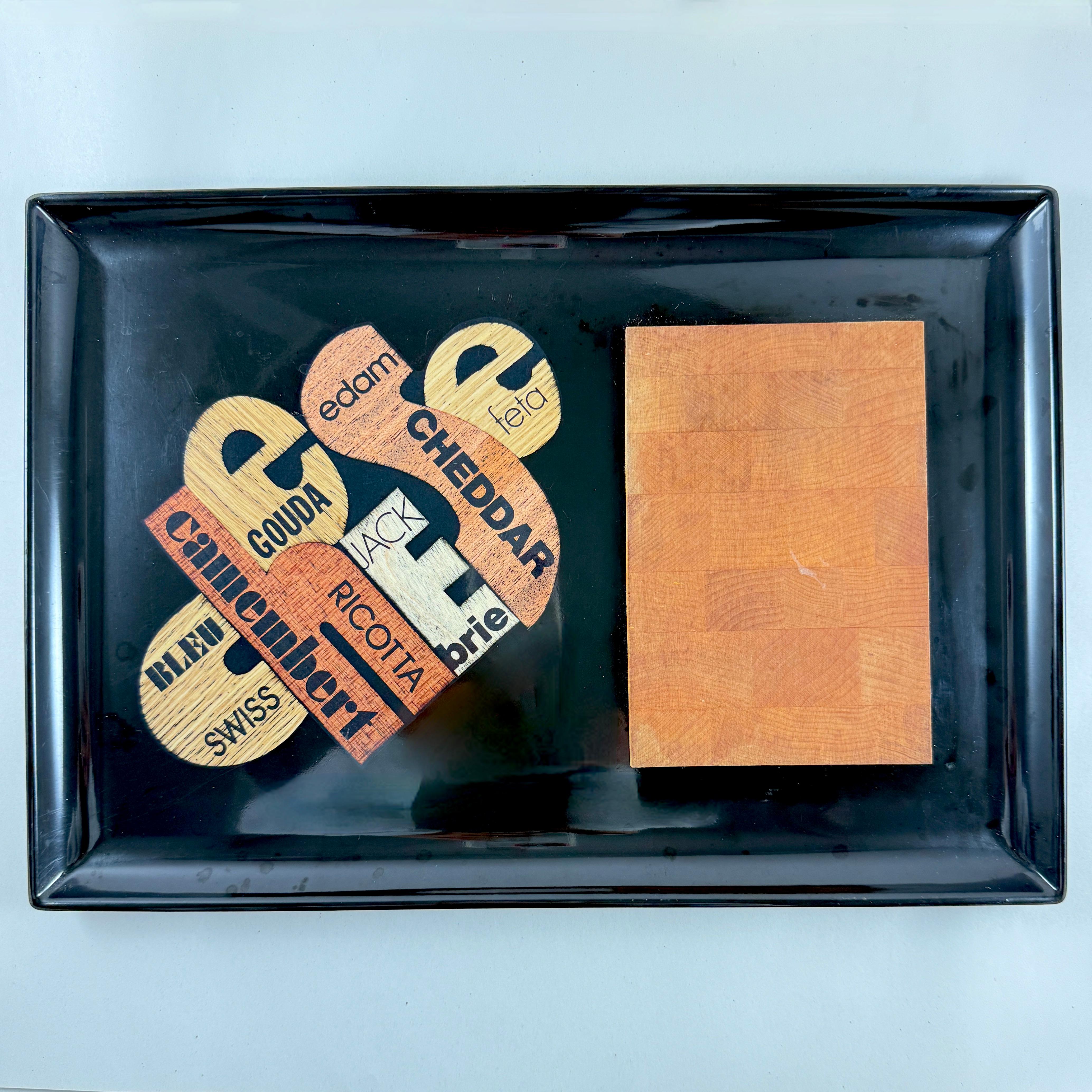 A Mid-Century Modern Era cheese board tray by Couroc of Monterey, California (1948-1998) – circa 1960s.

Made of a black resin called ‘Phenolic’ and hand inlaid with natural woods and a hardwood cutting surface made of New England Sugar Maple.
The