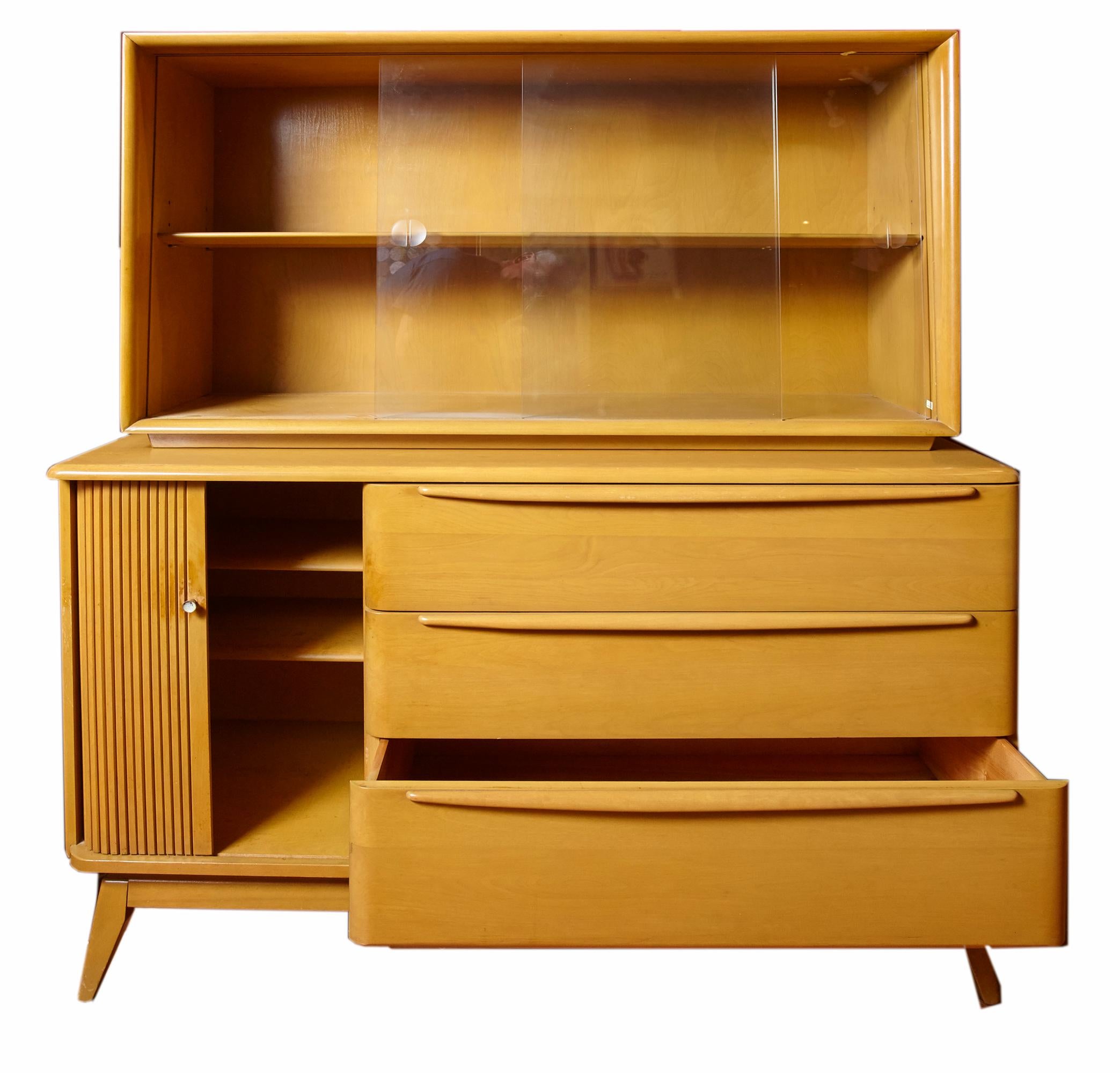 Midcentury birch credenza and hutch with 'Champagne' finish by Heywood Wakefield from the 1950s. Lower part has three drawers on the right and tambour door on the left enclosing 2 shelves. The upper hutch has sliding glass doors and 1 shelf. In