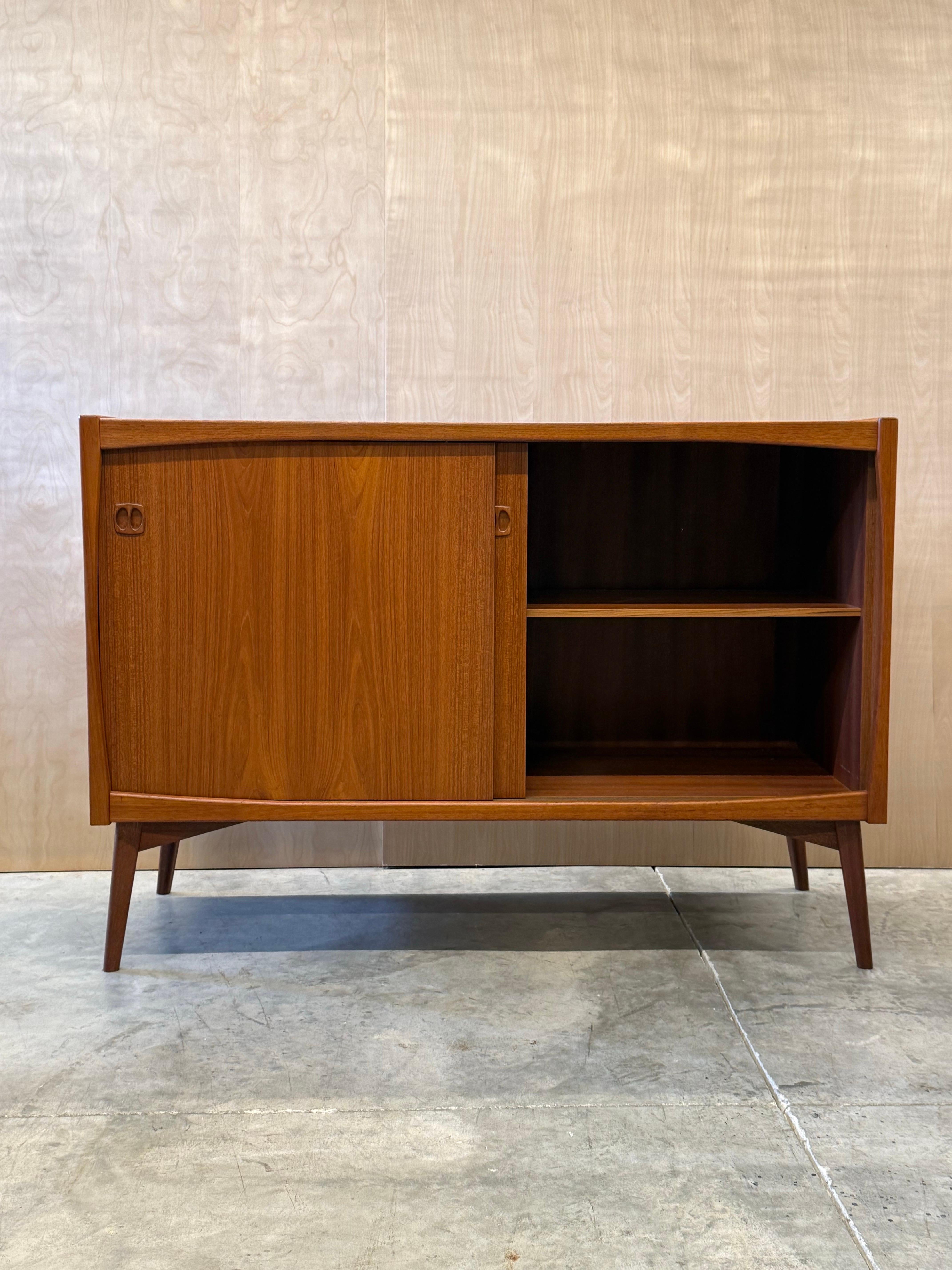 Mid-century compact credenza. Designed by Laurtis M. Larsen and made from teak wood. This piece features two smooth sliding doors that align the front of the credenza. The handles are carved inset and uniquely Danish. Both the left and right side