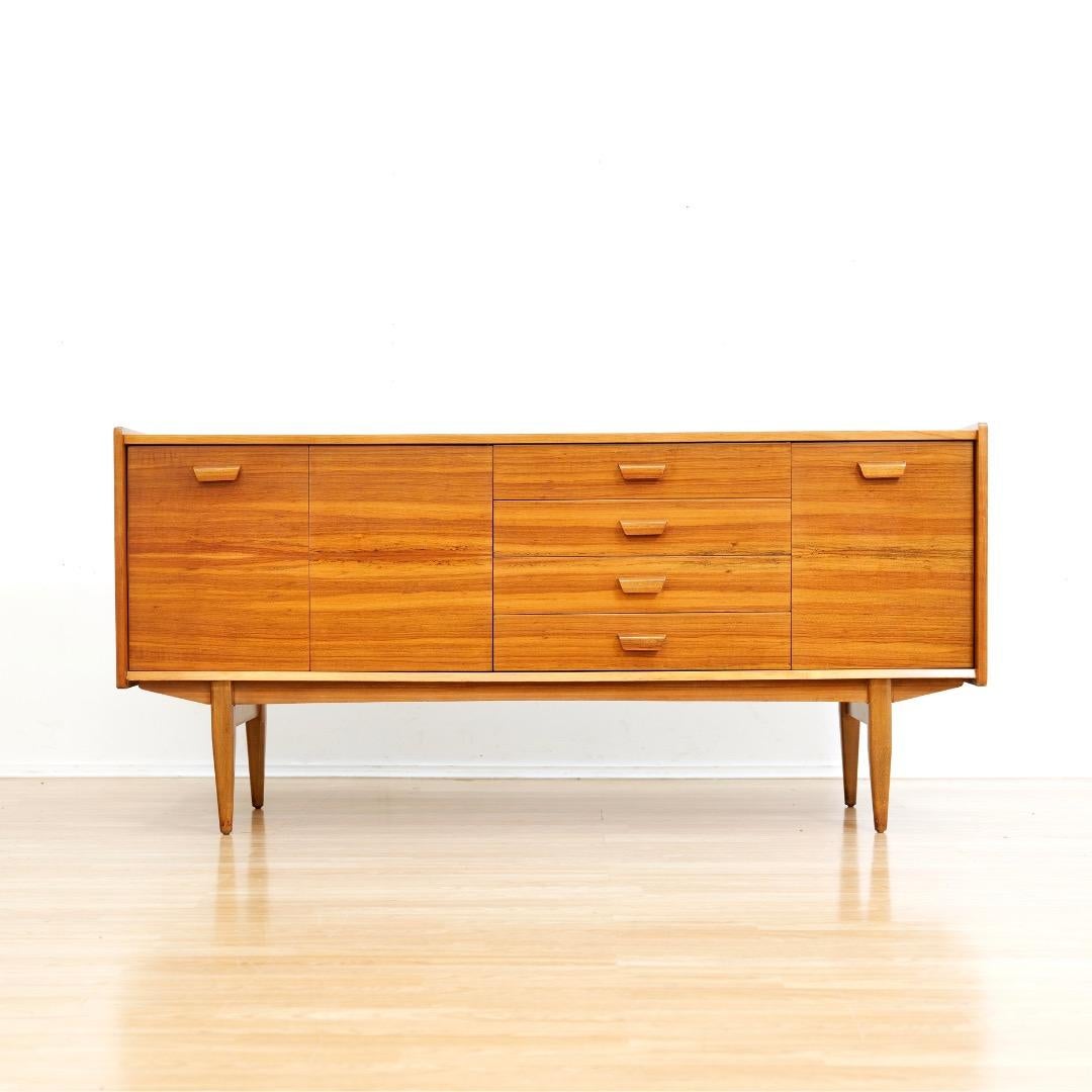 Cette crédence du milieu du siècle a été produite par Uniflex Furniture dans les années 1960. Avec son superbe grain d'allumette à l'avant et son design d'influence scandinave, il est typique de l'époque.  Avec ses quatre tiroirs flanqués d'étagères