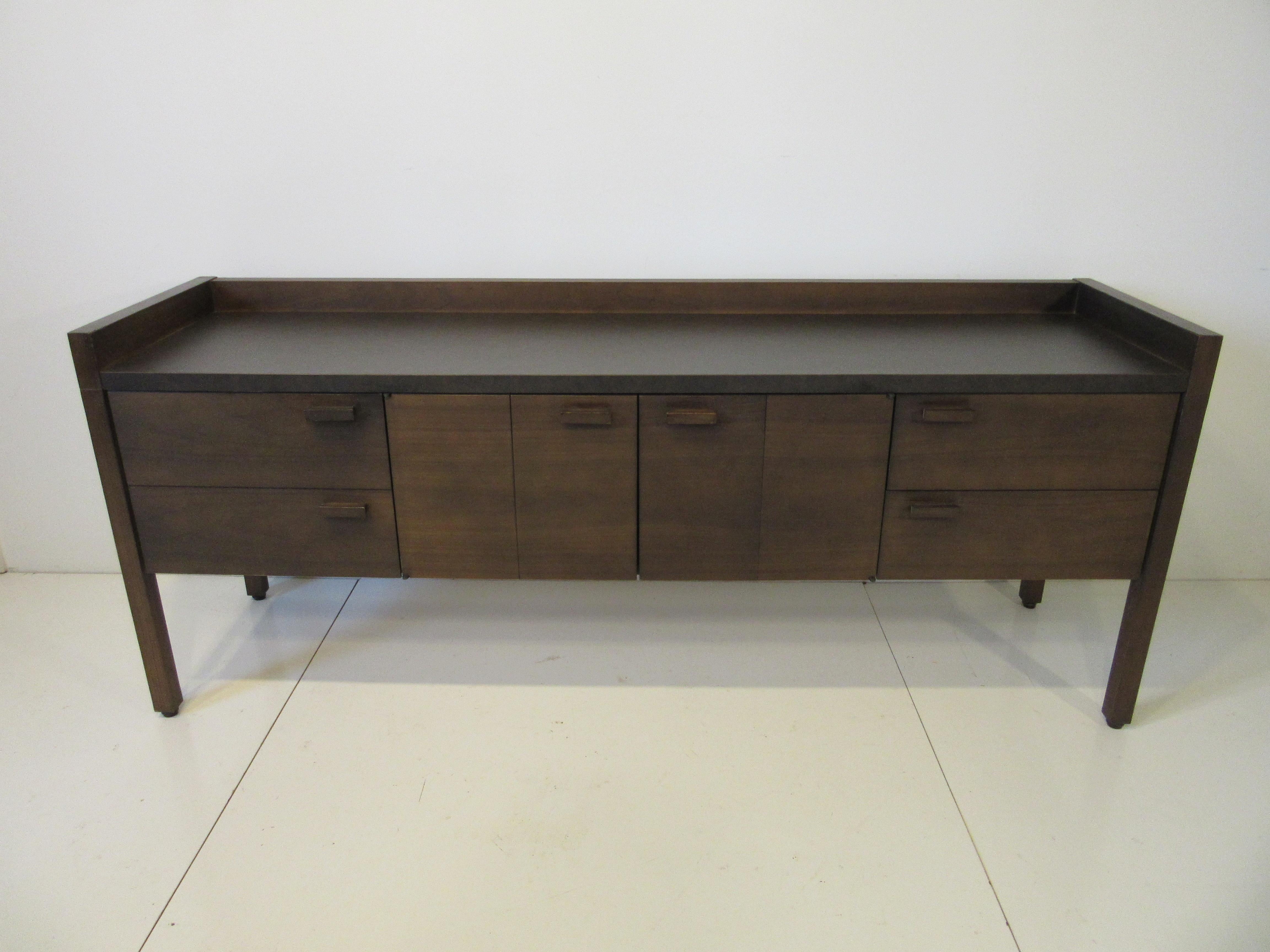 A dark toned mid century sideboard / credenza with one large drawer to the left side and two drawers with movable dividers to the right , the middle has two bi fold doors , storage and an adjustable shelve . The handles are a matching wood and the