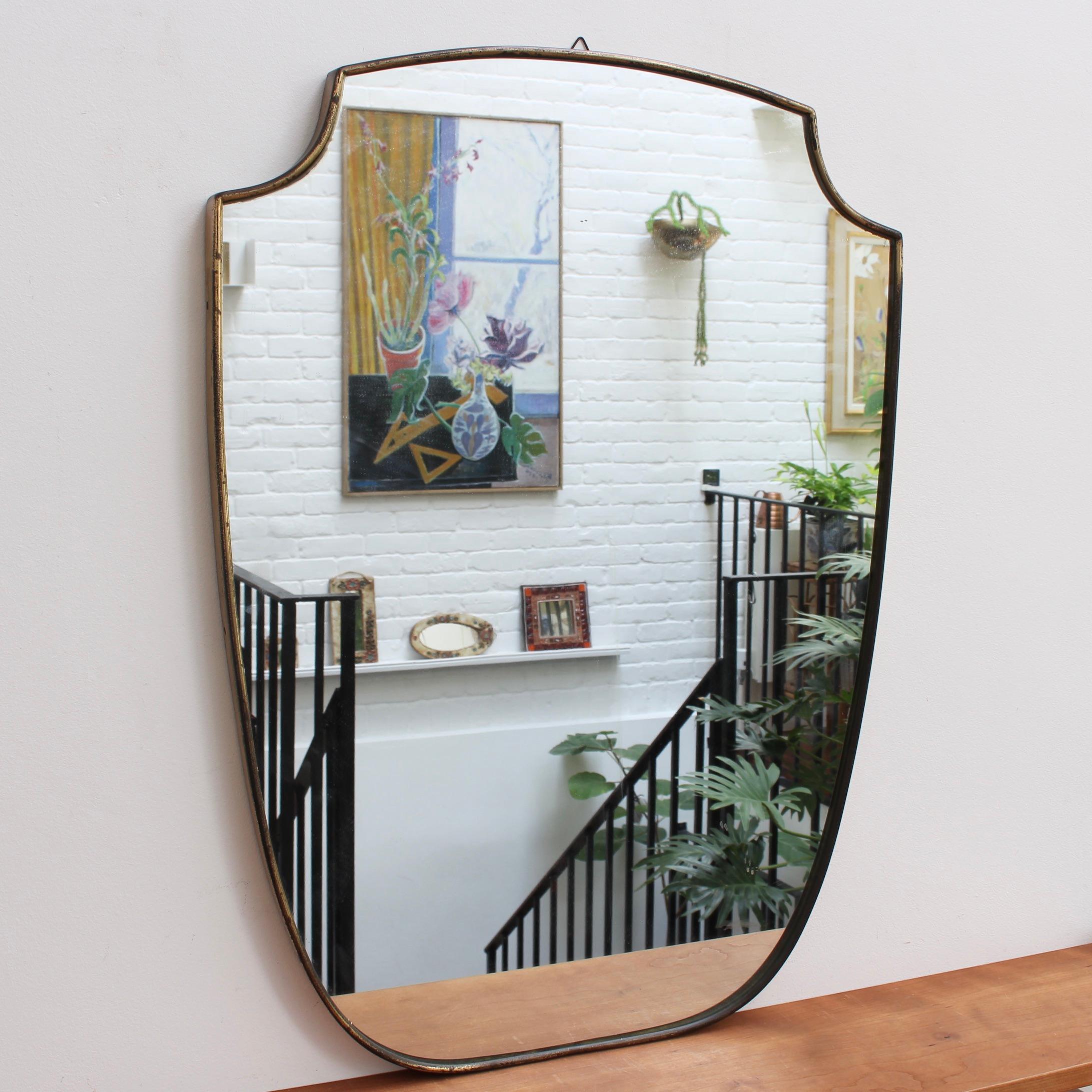 Vintage Italian wall mirror with brass frame (circa 1950s). The mirror is substantial, crest-shaped - classically elegant in a modern Gio Ponti style. Overall, the piece is in fair vintage condition presenting an aged, dark patina and evident