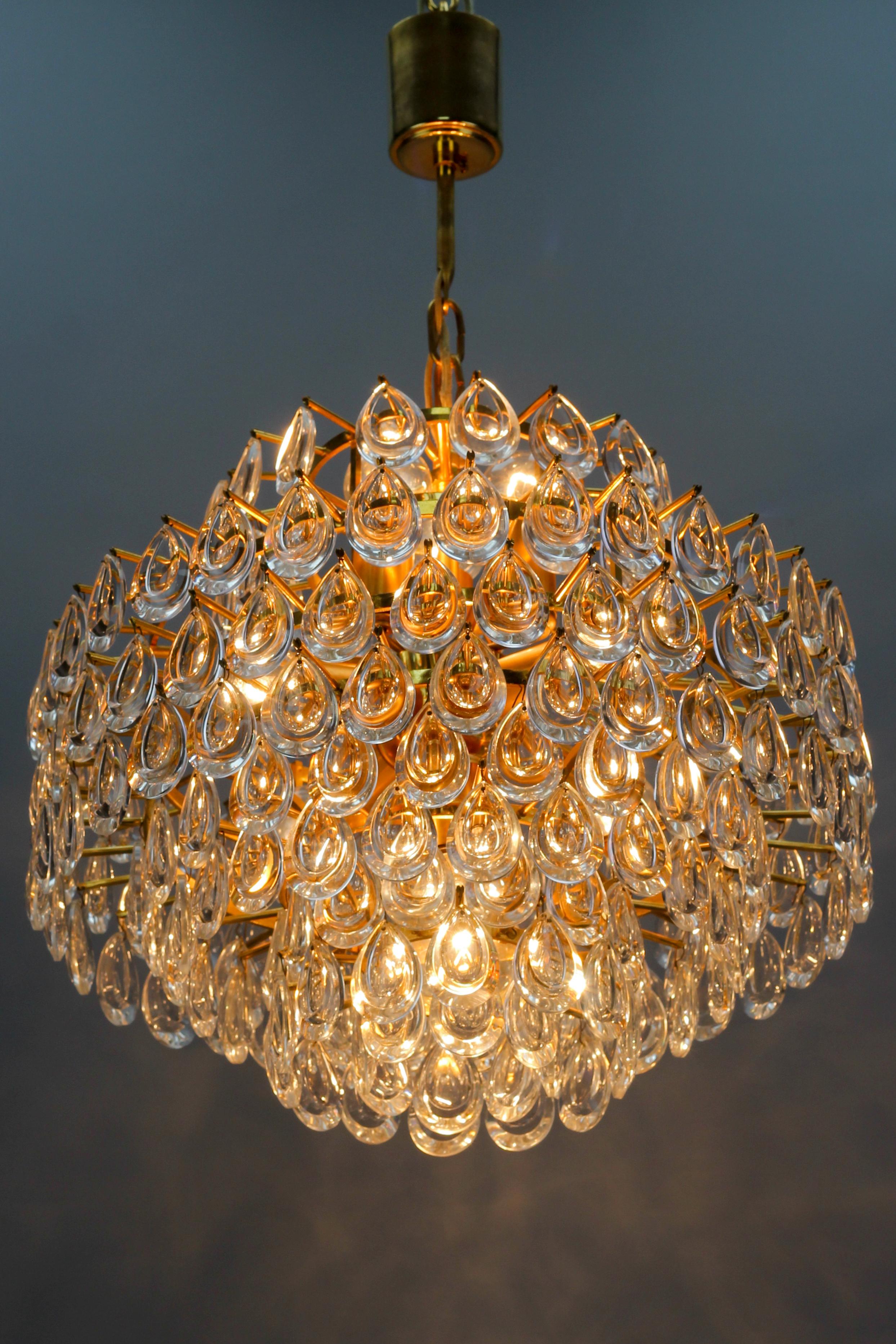 This impressive seven-tier chandelier by Palwa, manufacturer Palme & Walter, Germany, 1960s, features a gilded brass frame with 208 (+3 reserve) teardrop-shaped crystal glass prisms - lenses. 
Seven light points - six sockets for E14 and one socket
