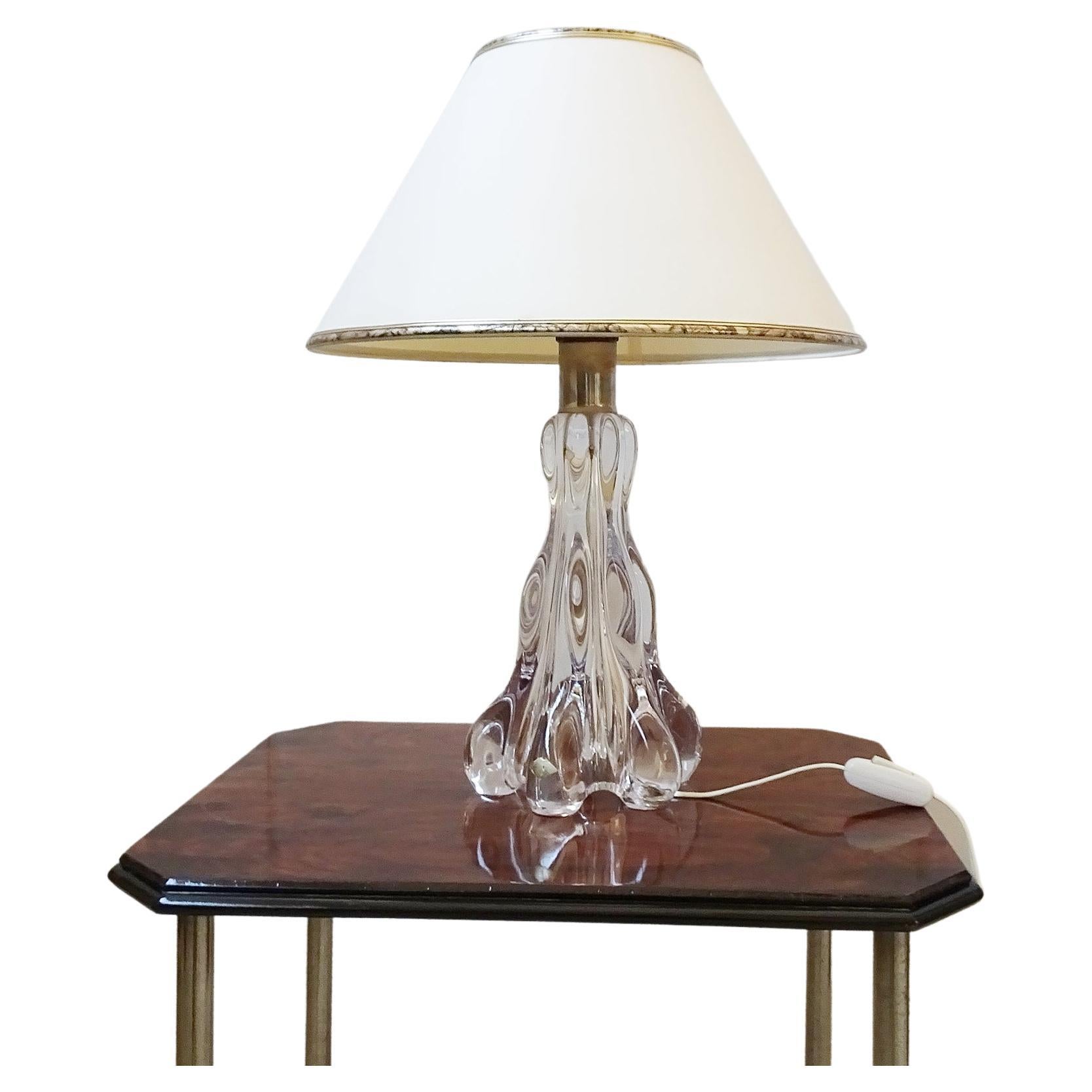 French table lamp by Glashütte Vannes le Chatel. The sculpturally shaped base made of crystal glass has six protruding wavy edges and gives a brutalistic but noble look. Finished off with a cream colored lampshade with a gold colored abstract
