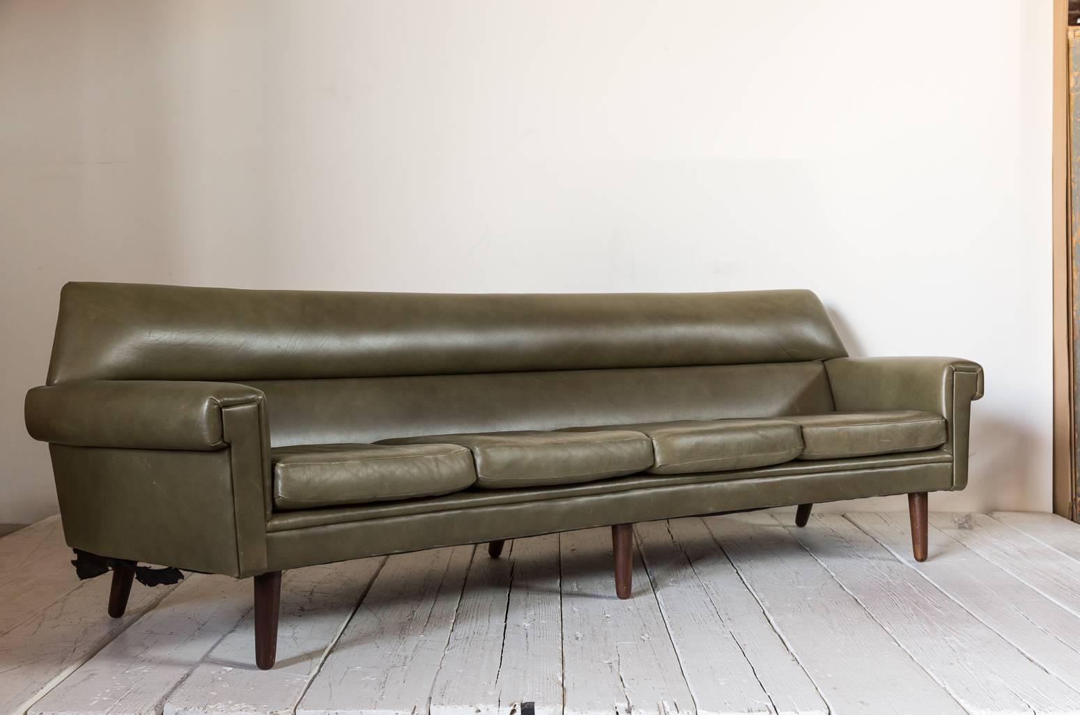 Midcentury olive green leather sofa with a slightly curved back with a tapered cylindrical leg and four loose cushions with a tight back.