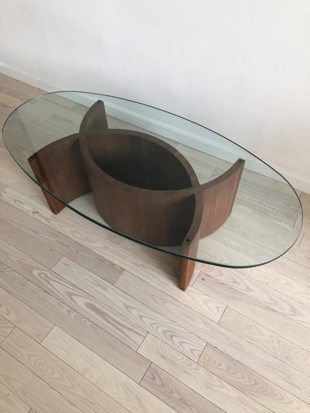 A stunning curvy sculptural walnut based coffee table with glass top. Incredibly clean and sleek. An excellent addition to your modern or eclectic home. One small chip in glass, and a few nicks in walnut base, as pictured.

Measures: 25.25