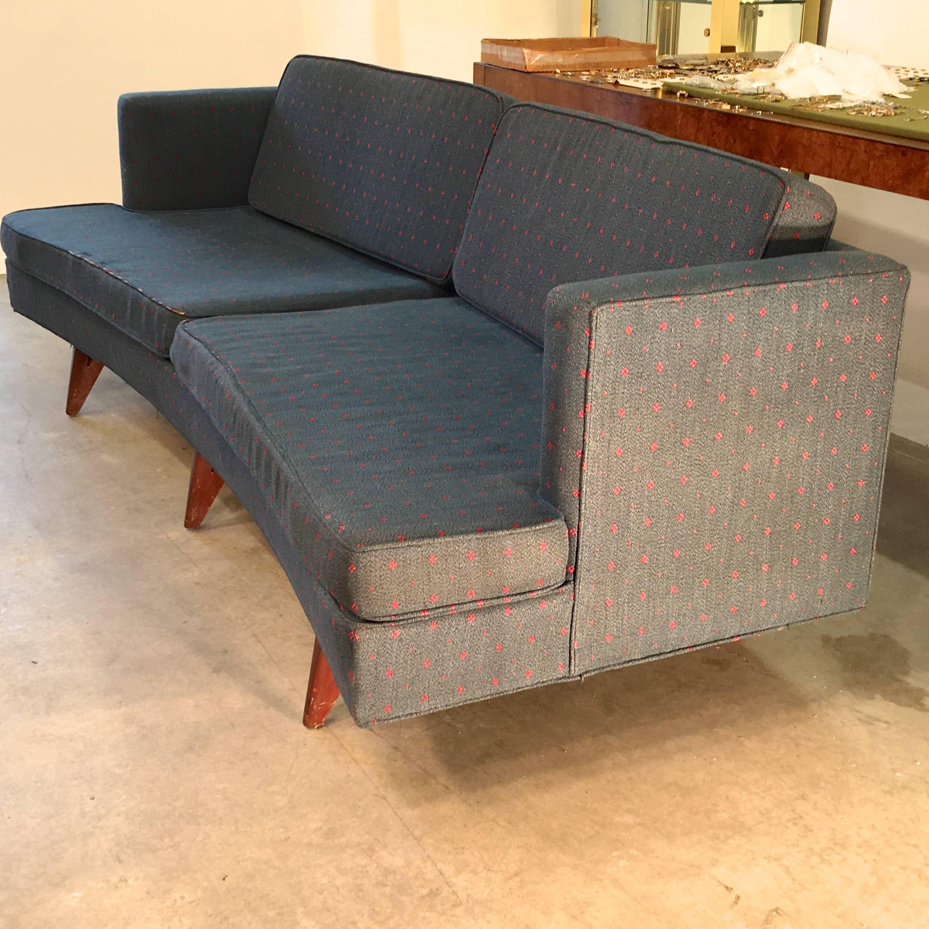 Midcentury curved sofa (front and back) with half track arms, on six distinctive V-form walnut stained legs artfully positioned on a rakish angle, circa 1960. Two split notched edge seat cushions and two loose back cushions. Apart from the legs the