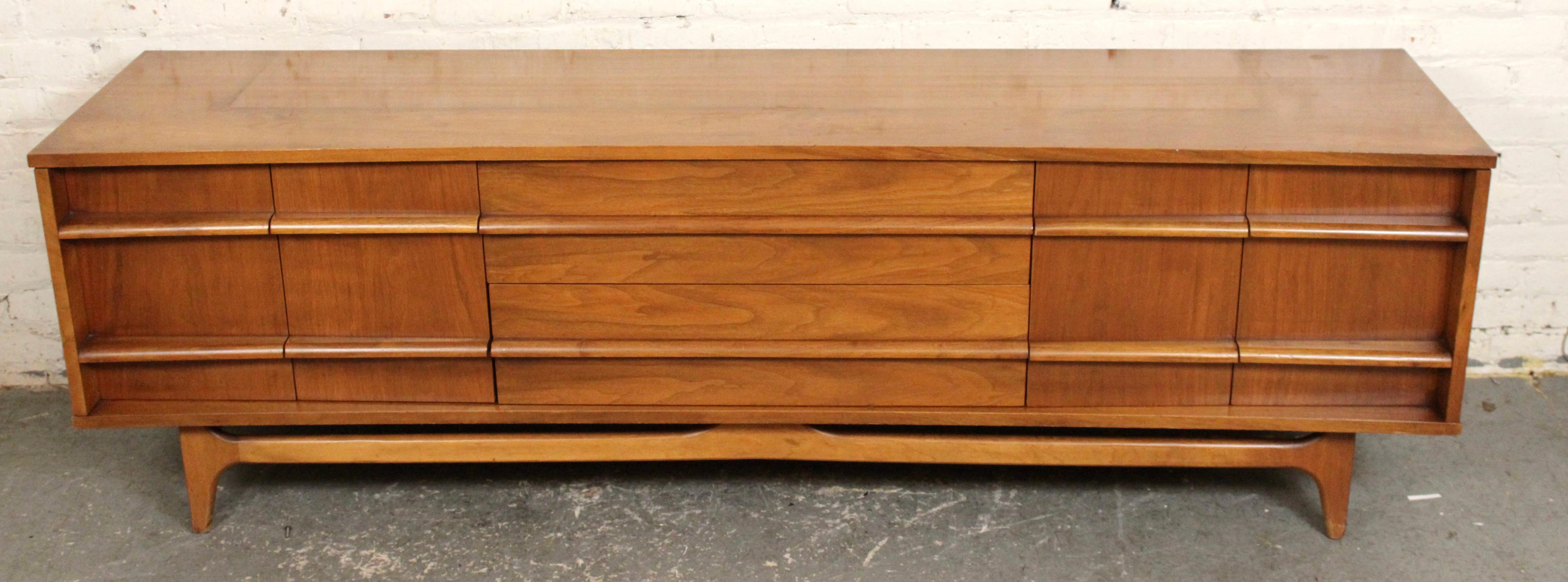 A striking mid-century modern dresser crafted by Young Manufacturing Company, circa 1960s. This piece features rich walnut construction with signature sculpted drawer fronts and clean architectural lines. The warm wood grain is beautifully showcased