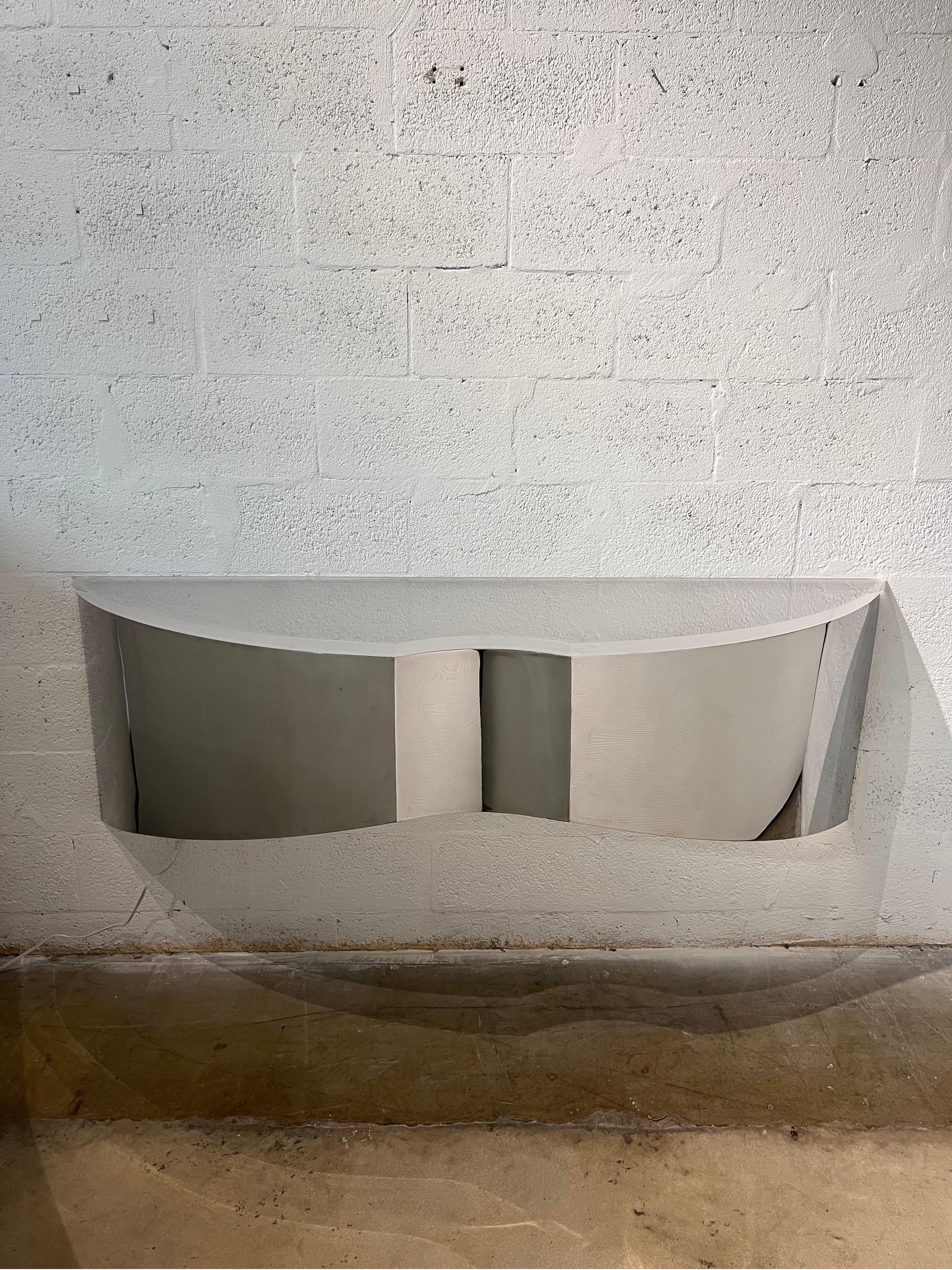 Custom polished steel floating wall console or shelf with frosted lucite top circa 1970s.  A welded steel bracket on the interior holds a new LED tube lamp that can be hardwired or plugged into a wall socket.  