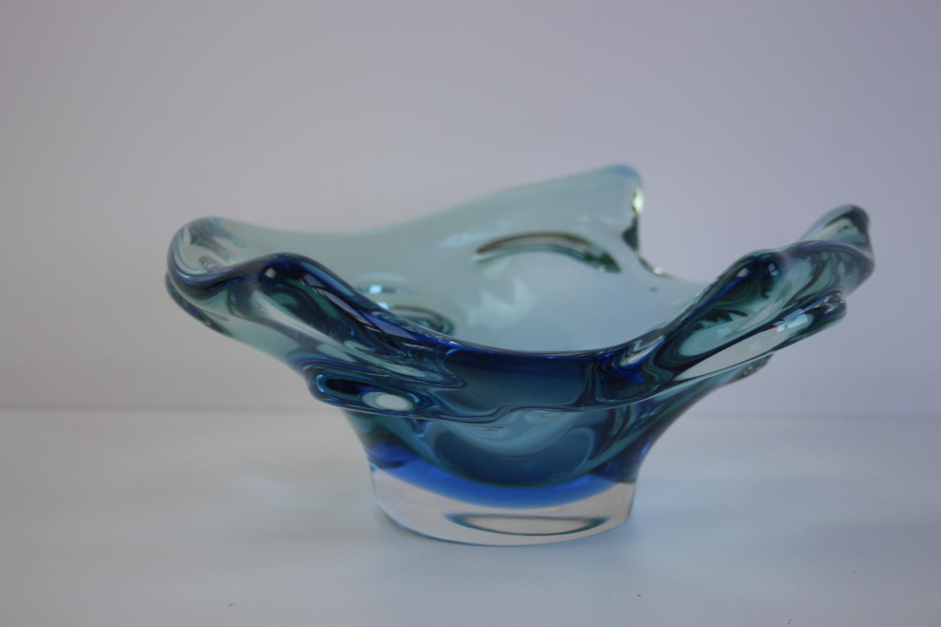 A striking hand-blown art glass bowl designed and produced by Chřibská Glassworks in Czechoslovakia during the 1960s. This sculptural piece features dramatic, flowing organic lines with layered tones of deep blue and emerald green, captured in