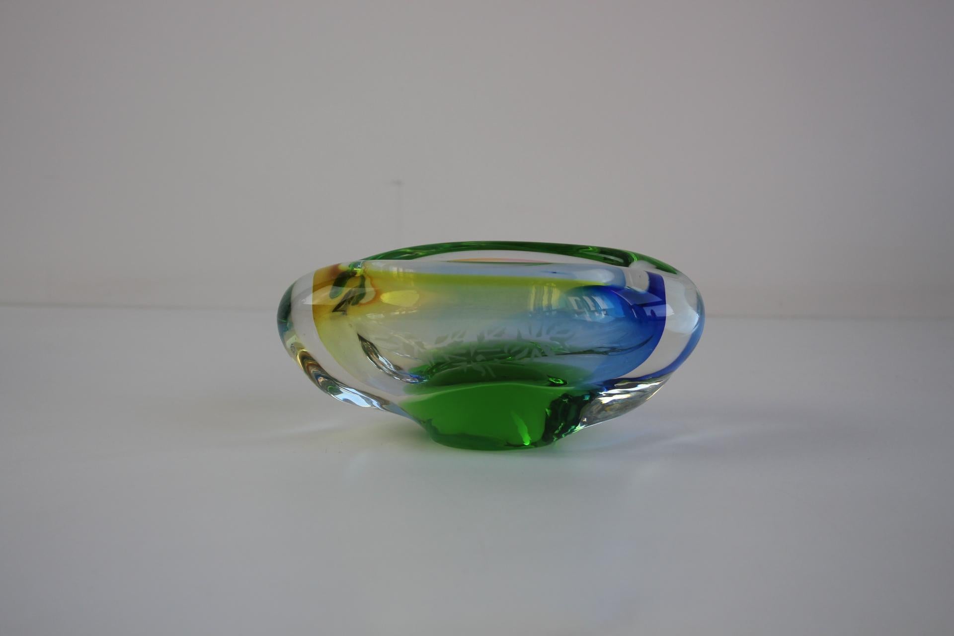 A stunning mid-century modern ashtray made of heavy Bohemian art glass using the sommerso technique. Hand-shaped in Czechoslovakia in the 1960s, this piece features bold, layered colors—emerald green, amber, and deep blue—encased in thick, clear