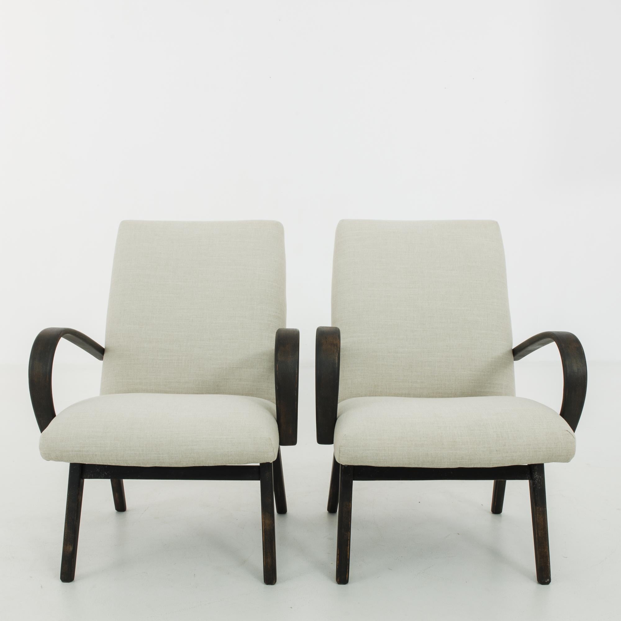 This pair of upholstered wooden armchairs was made in Czechoslovakia, circa 1960. Bentwood armrests and tapered, splayed legs give the chairs an expressive silhouette. The newly upholstered seats and backs come in a calming pale gray tone,