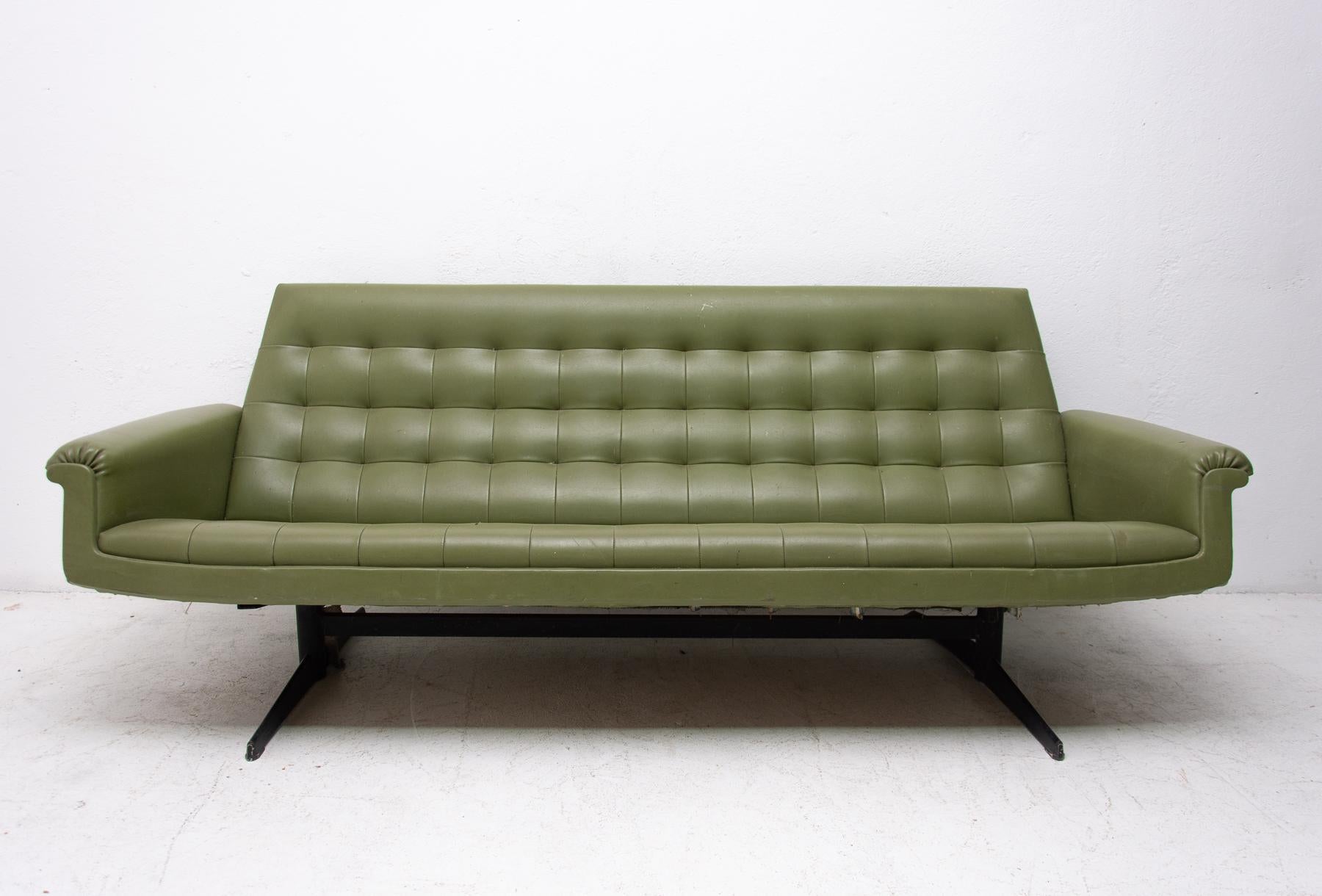 This sofa was made in the former Czechoslovakia in the 1970 as a part of living room set consists of one sofa, pair of swivel armchairs and stool. The sofa is upholstered with green leatherette. The legs are made from iron. One leg is slightly bent