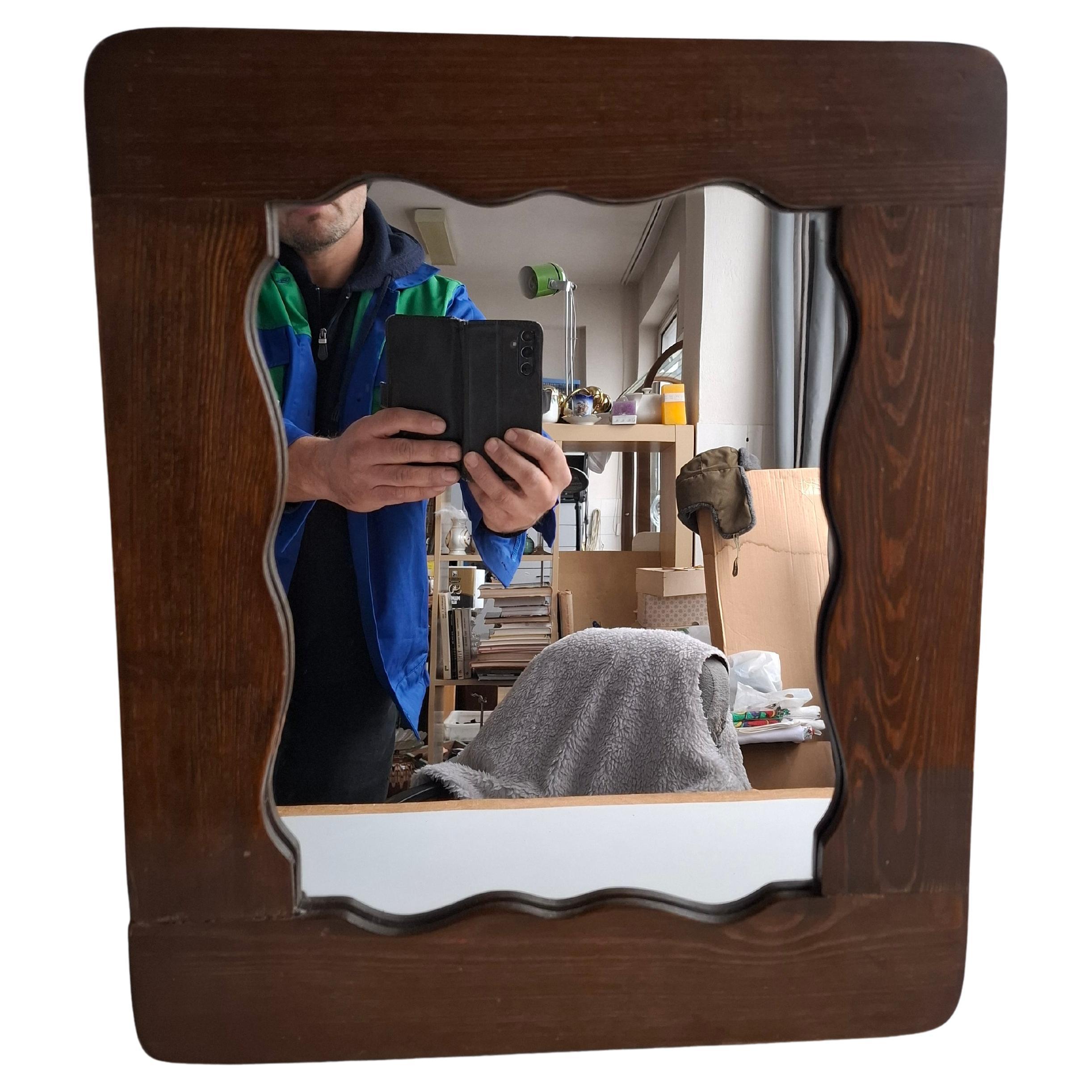 A striking mid-century wall mirror from 1940s Czechoslovakia, distinguished by its sculpted wavy wooden frame and original mirror glass. The piece shows an attractive, authentic aging patina that highlights its period craftsmanship. Ideal for