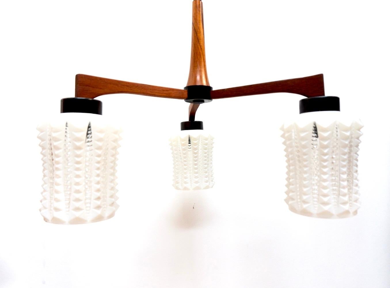 Auffällige dänische Trio Pendel-Deckenleuchte mit zylindrischen Schirmen, die eine  undurchsichtige weiße Glasschirme  mit Details aus Klarglas.  
Die Lampenschirme werden von einem Teakholzrahmen getragen, der mit den originalen schwarzen