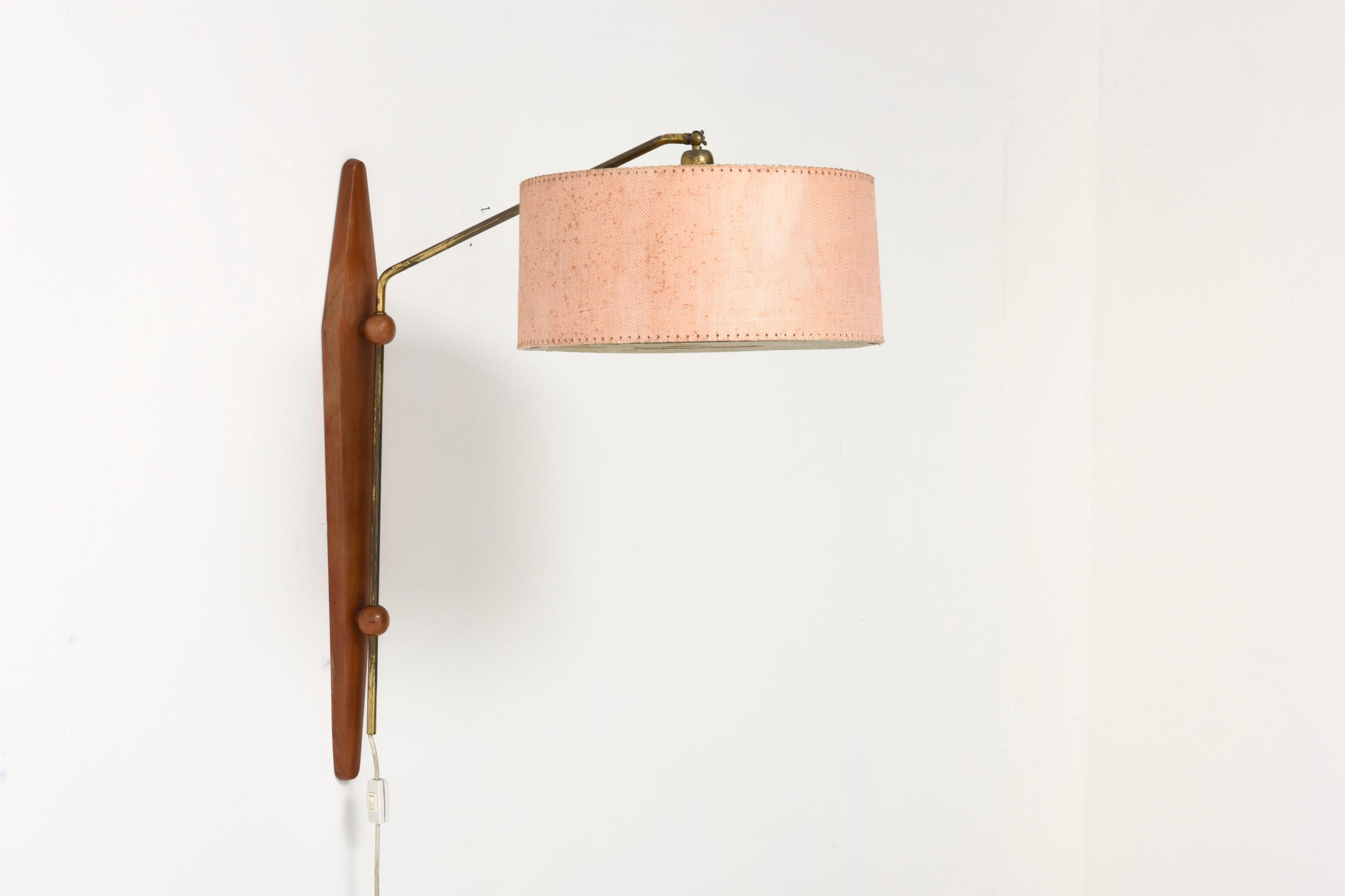 Adjustable teak wall lamp with brass elements and original fabric shade. A Danish wall lamp, original from the 60s. It has a sober and extremely refined design in teak wood, consisting of a pivoting arm, allowing us to carry the point of light to