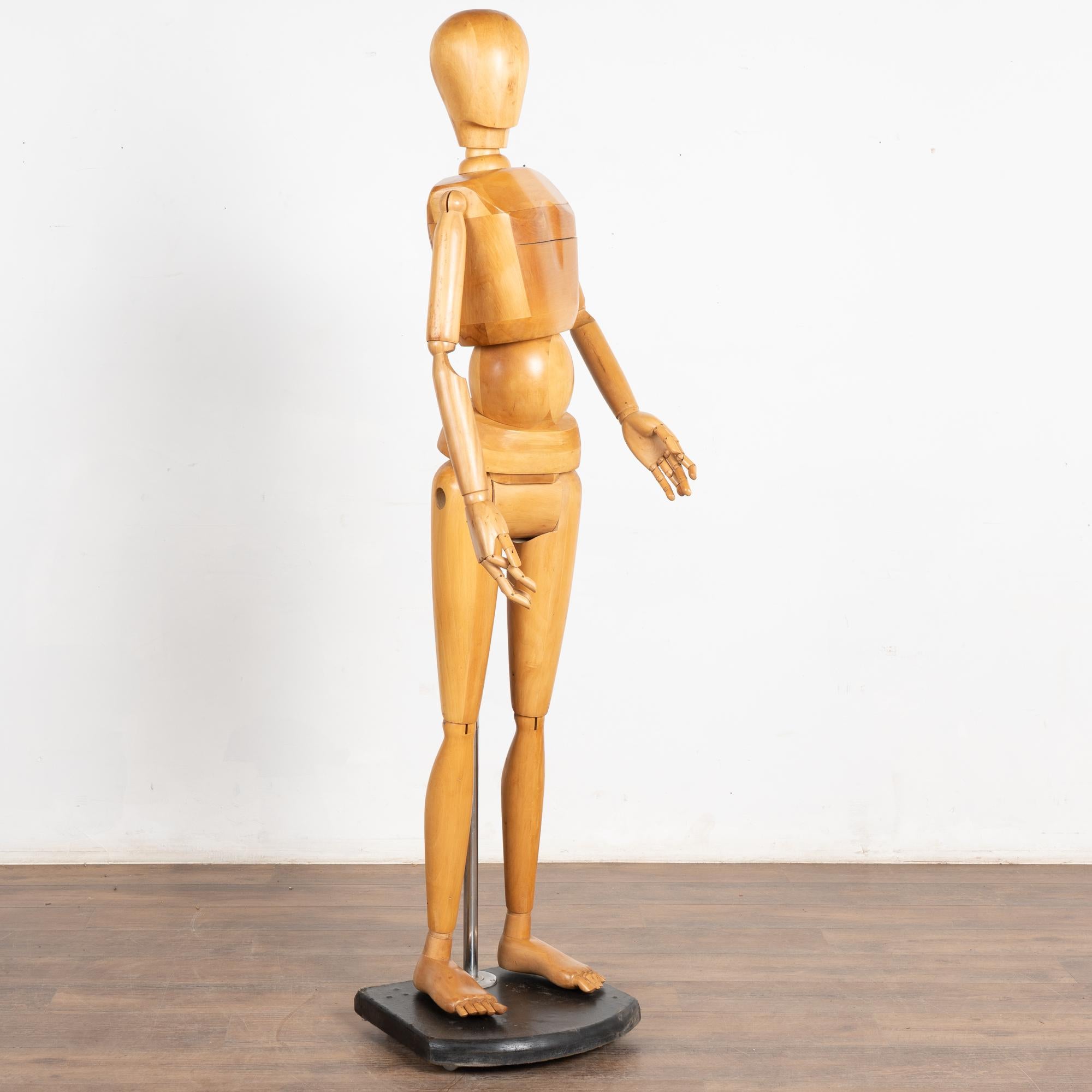 Un manichino o modello articolato per artisti a grandezza naturale della metà del secolo scorso, realizzato in legno massiccio. Un'asta metallica si attacca al retro della figura e alla base nera.
Può essere messo in posa in una varietà di posizioni