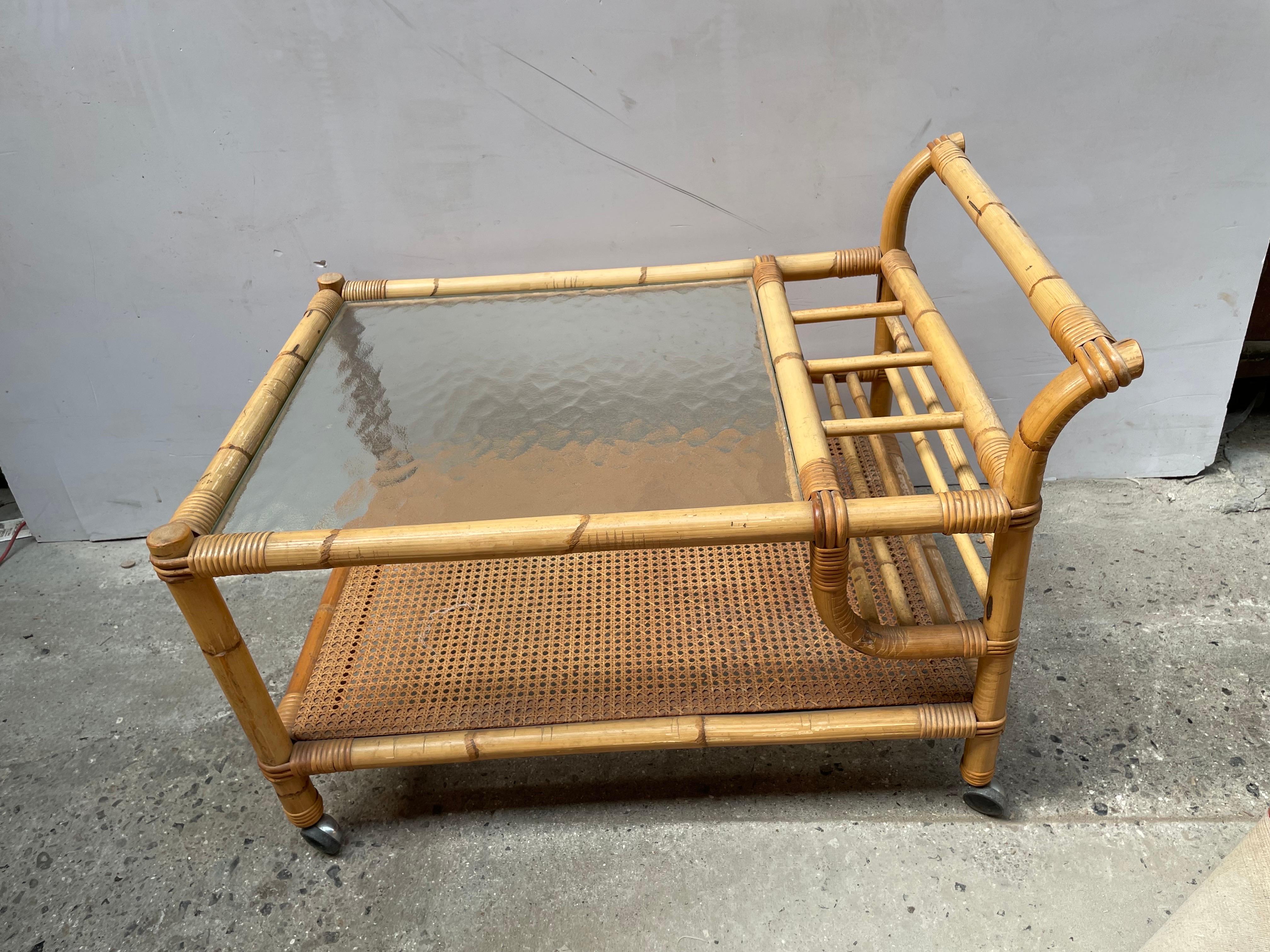 1960s vintage Mid Century Danish Bamboo Rattan Bar Cart. Crafted with exquisite attention to detail, this piece exudes timeless charm and functionality. Its bamboo and rattan construction evokes a sense of natural elegance, while the glass top adds
