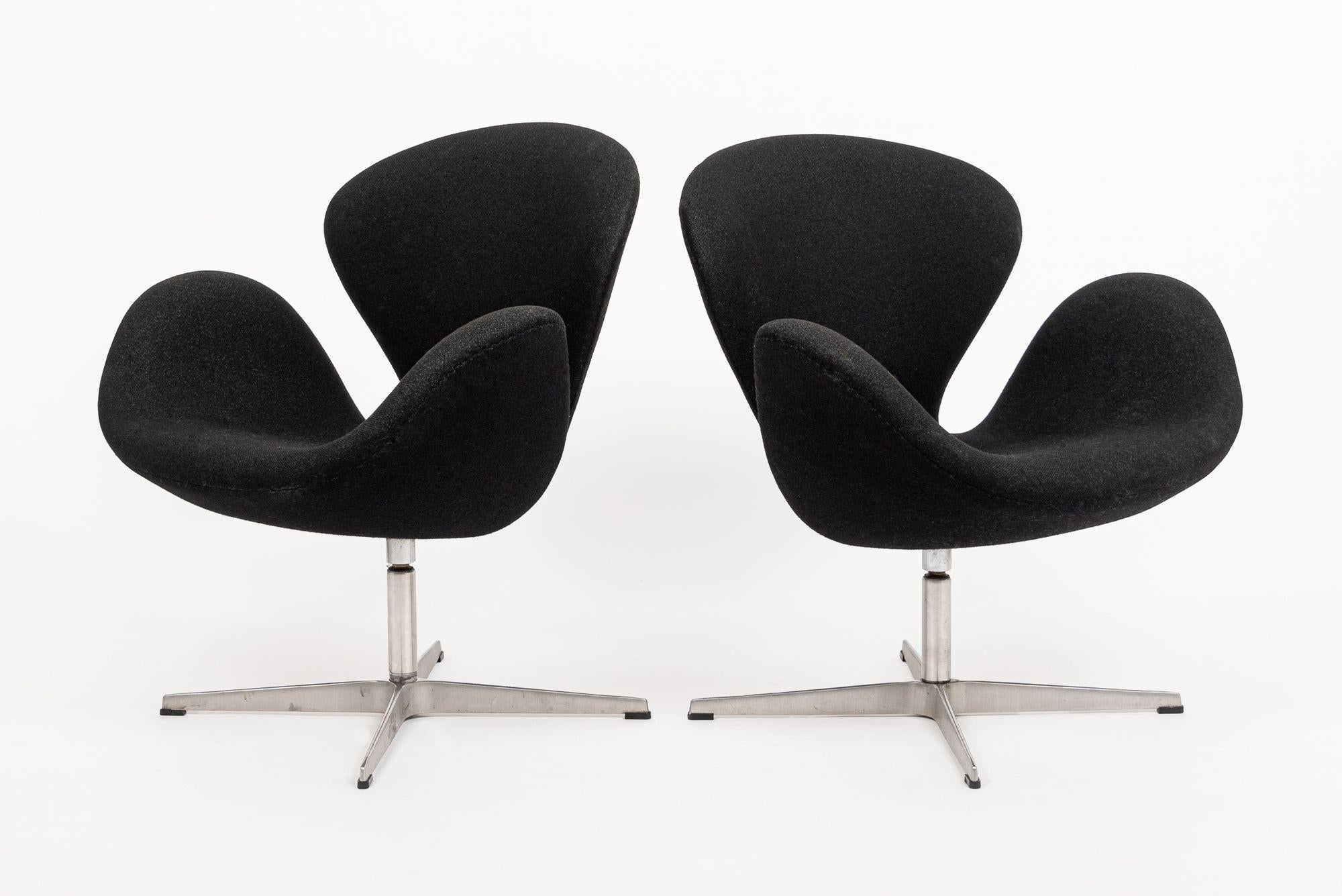 This gorgeous pair of vintage mid century Danish modern black Swan chairs by Arne Jacobsen for Fritz Hansen were made in Denmark and produced in 2002. They feature a 4-star aluminum swivel base and black woven upholstery. Both chairs retain Fritz