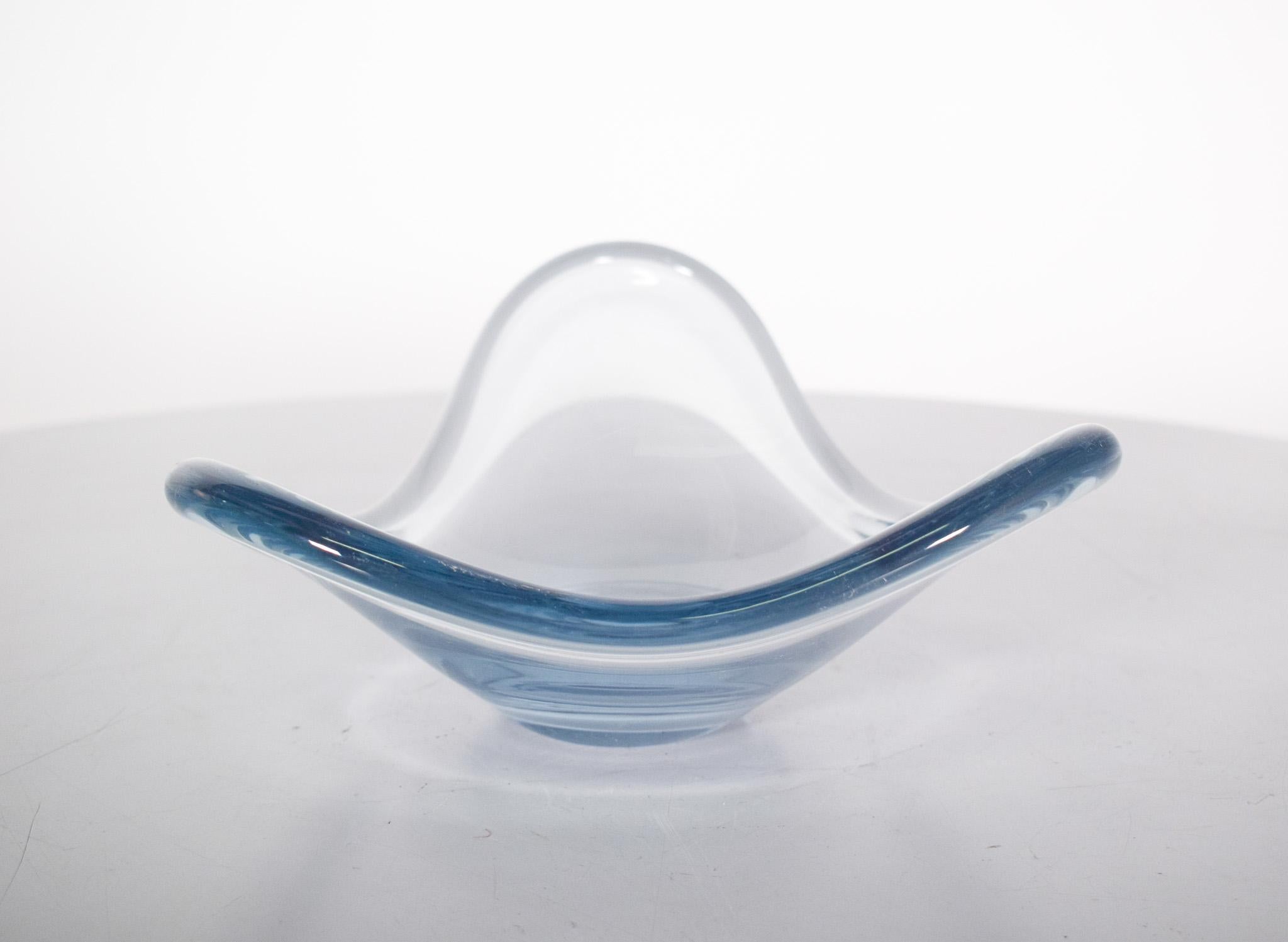 Blaue Glasschale. Die Form ist ungewöhnlich: Die Basis ist klein und rund, und aus der Mitte ragen drei längliche, runde Spitzen. Die Seiten fallen in einer sanften Kurve ab, wie offene Flügel. Es ist glatt, glänzend und sehr transparent. Das Glas