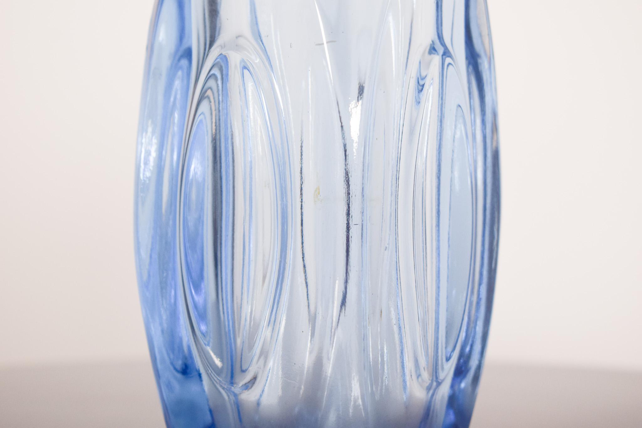 Vaso in vetro blu. Il corpo è ovale e leggermente contorto, con rilievi a forma di ellisse che creano interessanti riflessi e distorsioni alla luce. Il vetro è pesante e spesso, soprattutto alla base, il che conferisce stabilità al pezzo. 
La bocca