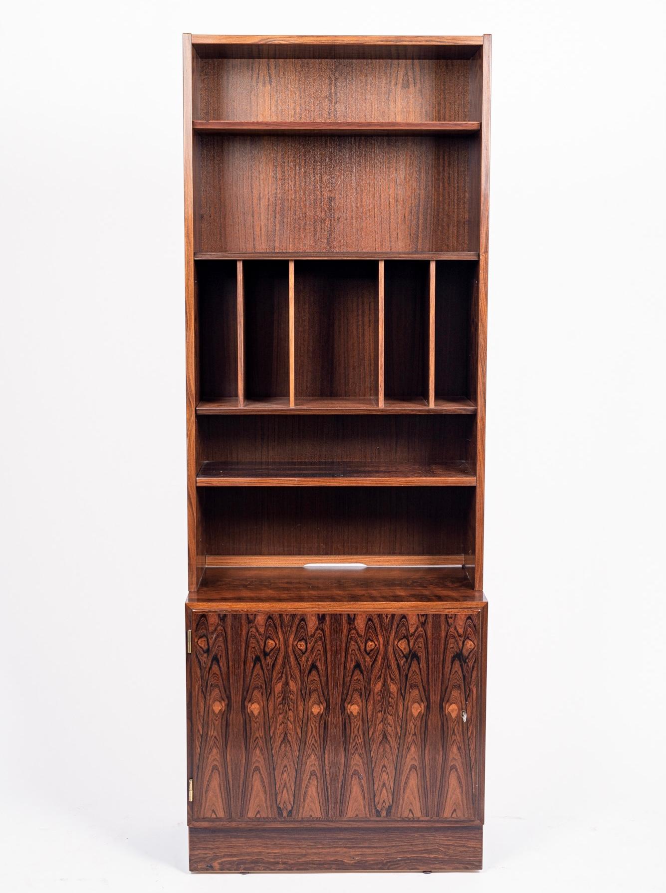 This vintage mid century Danish modern tall and slim rosewood bookcase was designed by Carlo Jensen for Hundevad & Co. and was made in Denmark circa 1960. The minimalist Scandinavian modern design features clean, geometric lines and the cabinet is